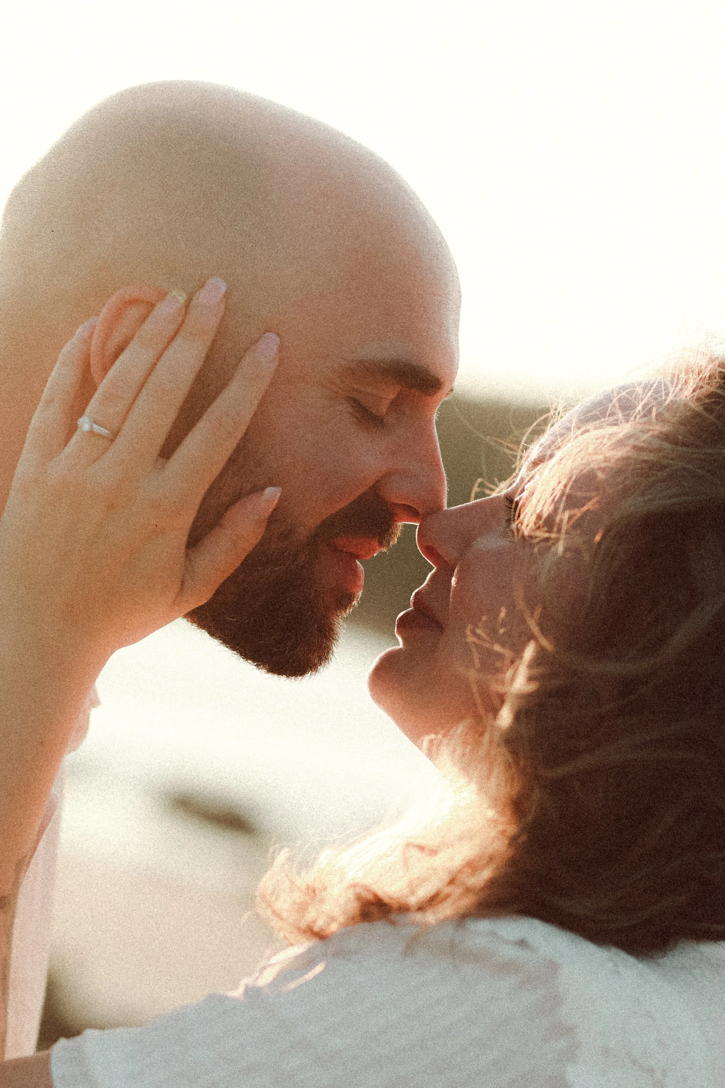 Un couple s'embrasse avec le front contre le nez, en lumière naturelle, ambiance romantique.