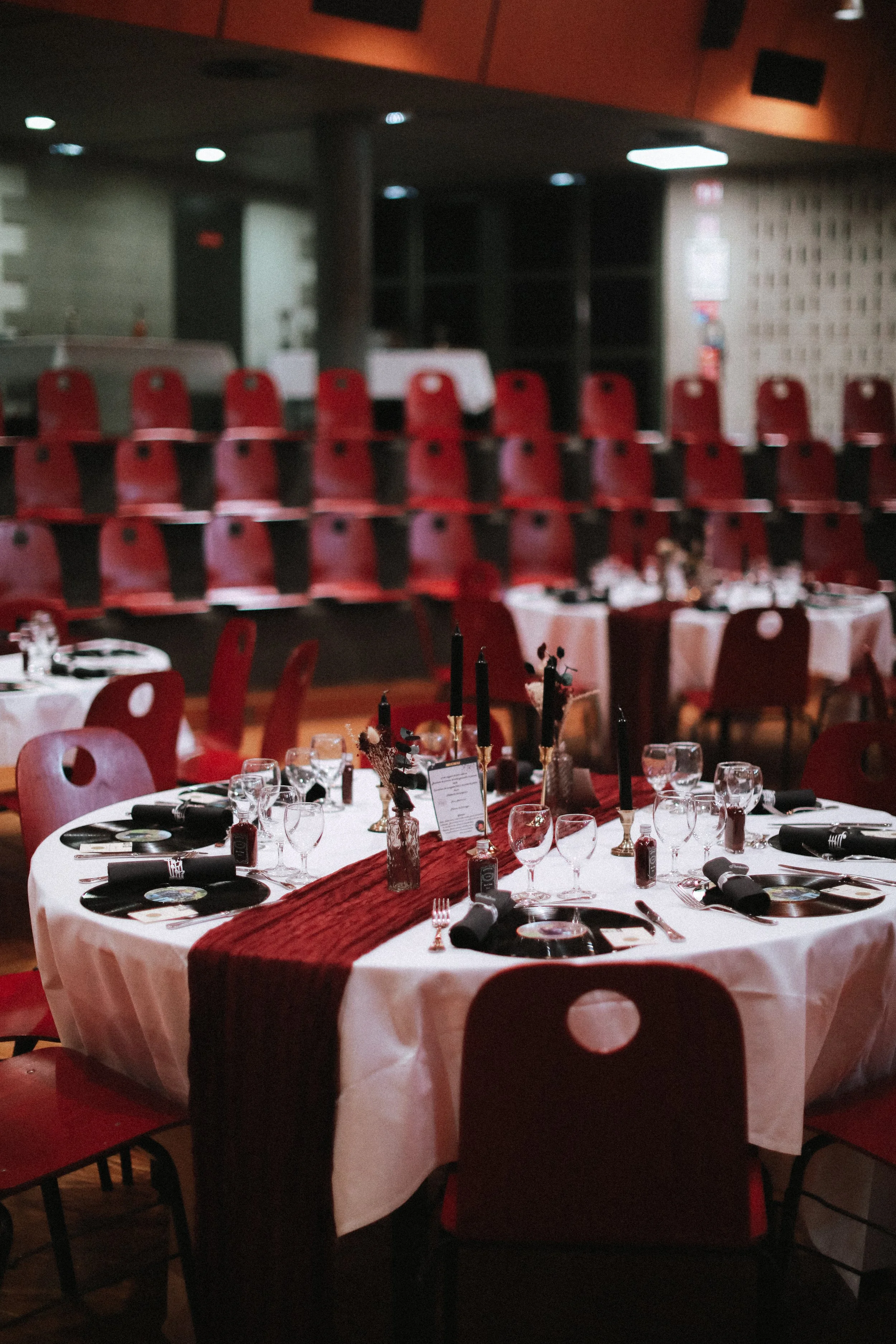 Table élégamment dressée pour un dîner de fête avec des chandeliers noirs, des verres, des assiettes et des couverts, dans une salle décorée en rouge et blanc, avec des chaises rouges.