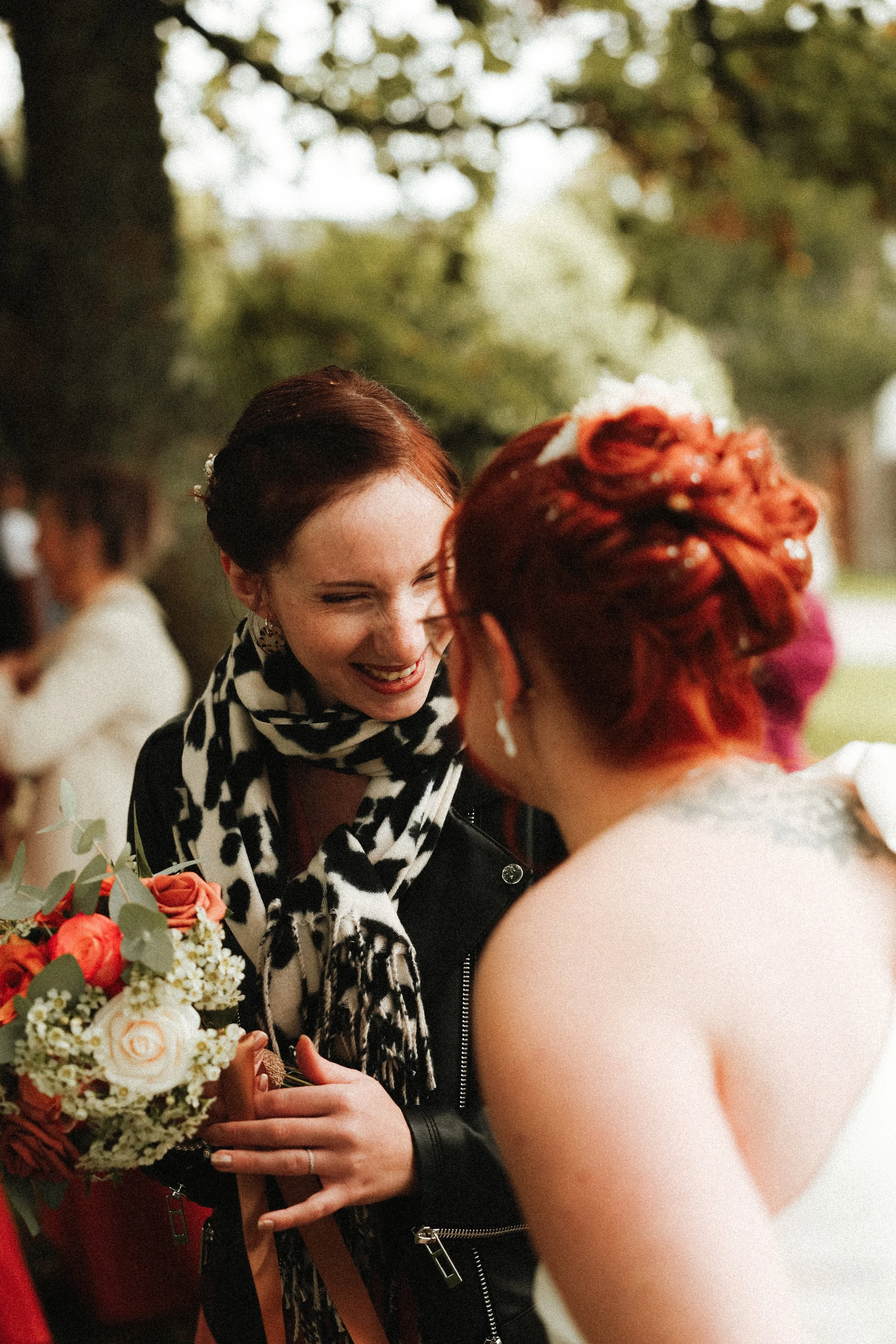 Deux femmes souriantes échangent lors d'un événement en plein air, entourées de personnes et de verdure.
