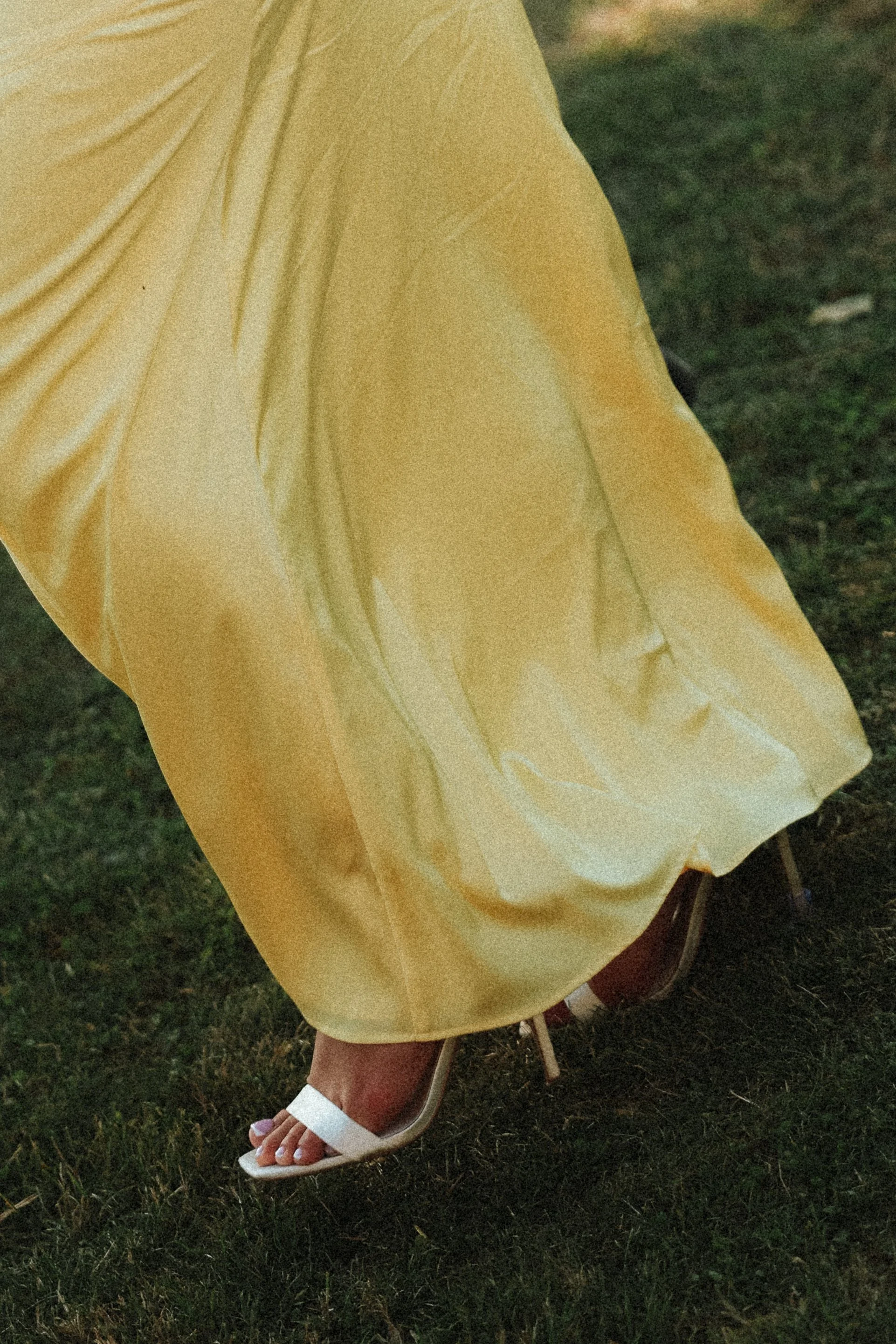 Une personne portant une robe longue jaune et des sandales blanches, marchant sur l'herbe.