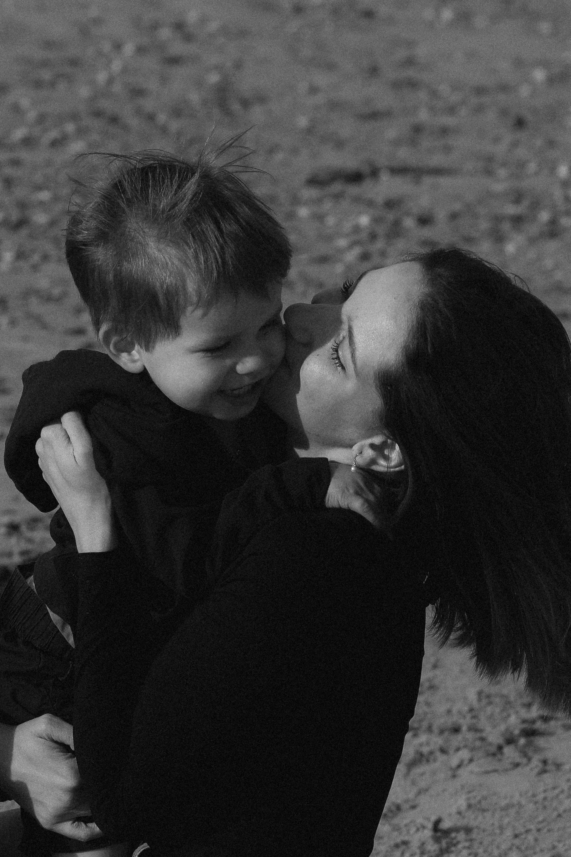Une femme et un enfant s'embrassent sur une plage, en noir et blanc.