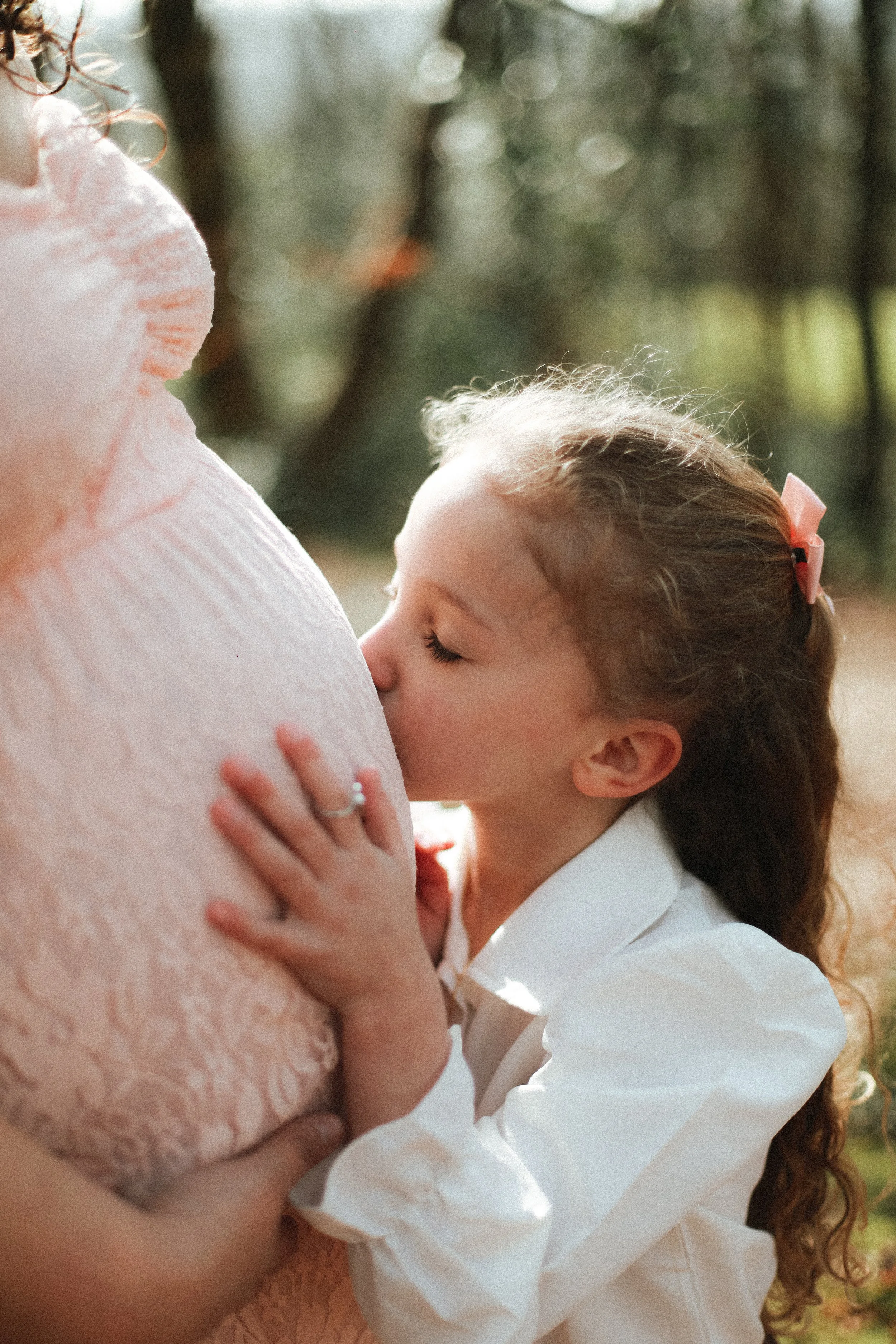 une jeune fille embrassant le ventre d'une femme enceinte dans un parc en plein air, entourée d'arbres