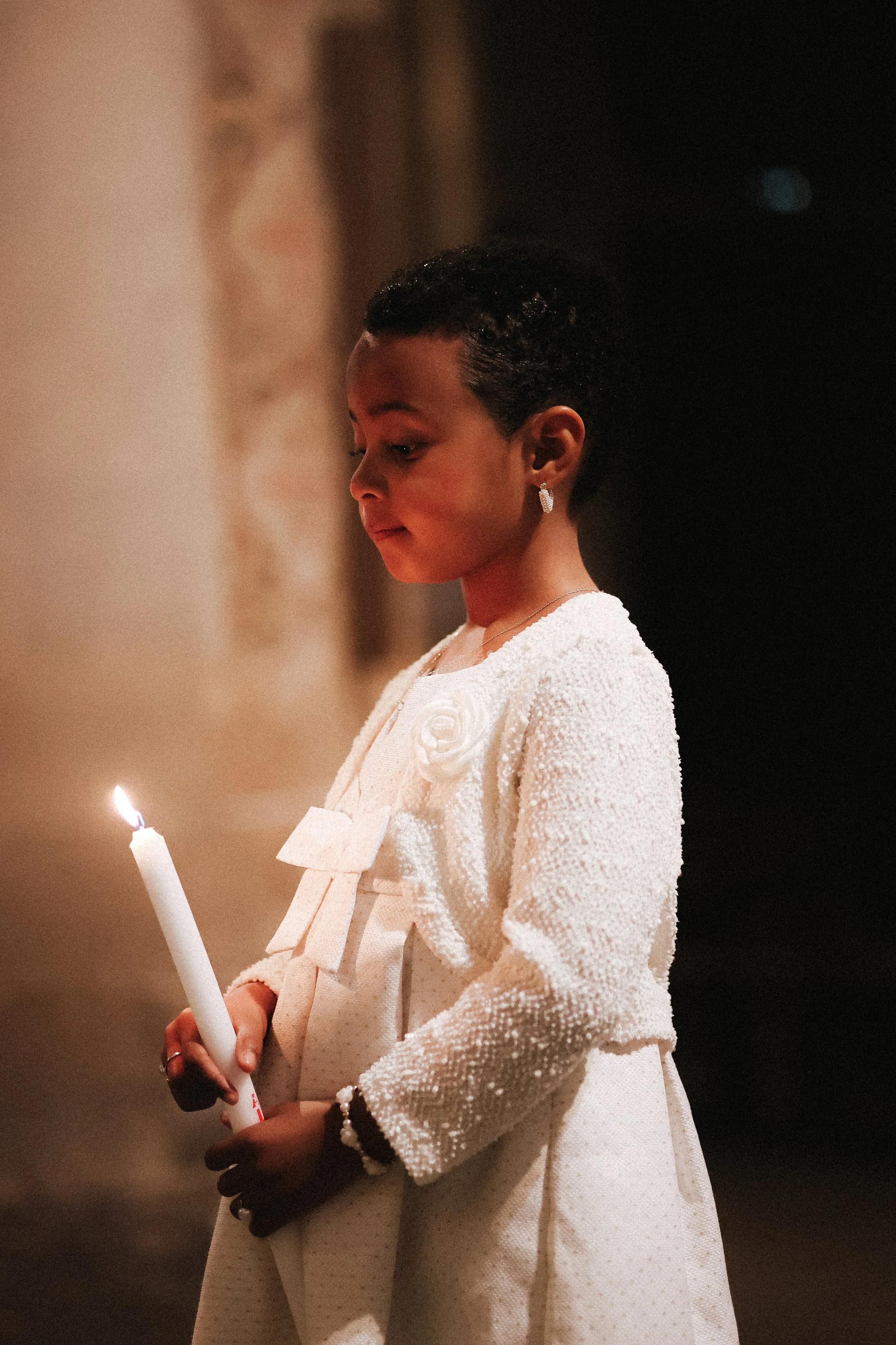 Une jeune fille noire habillée en blanc, tenant une bougie allumée dans un environnement sombre.