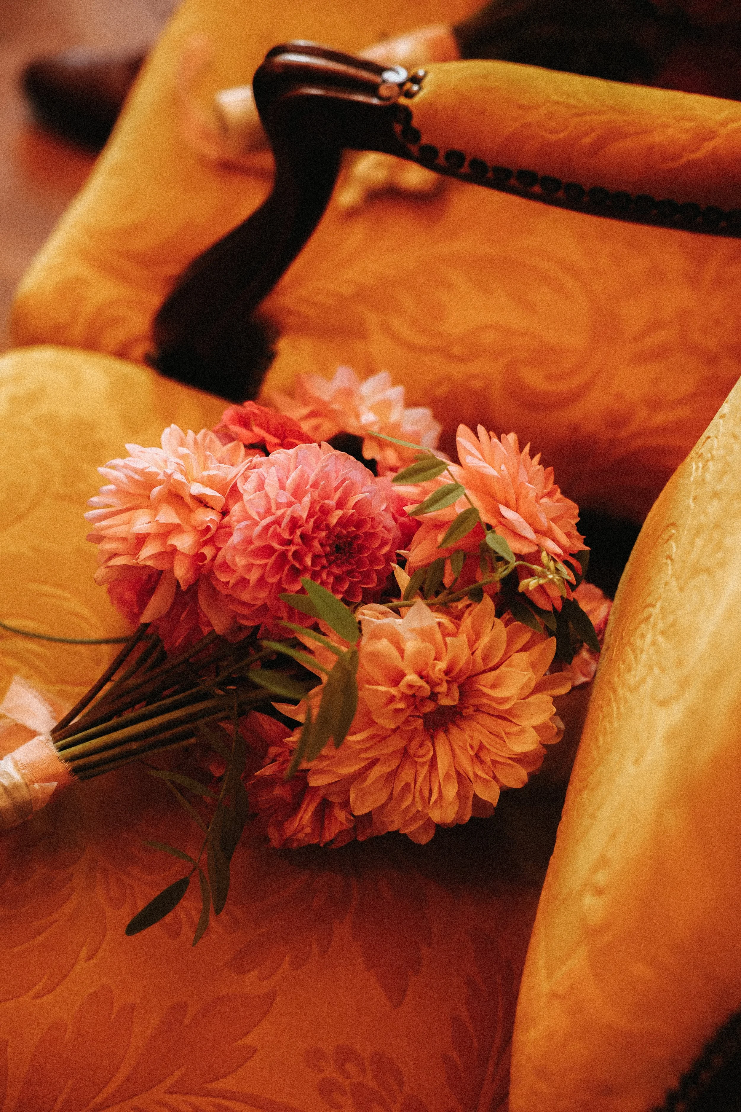 Un bouquet de fleurs roses et oranges posé sur un fauteuil en tissu jaune avec un motif floral.