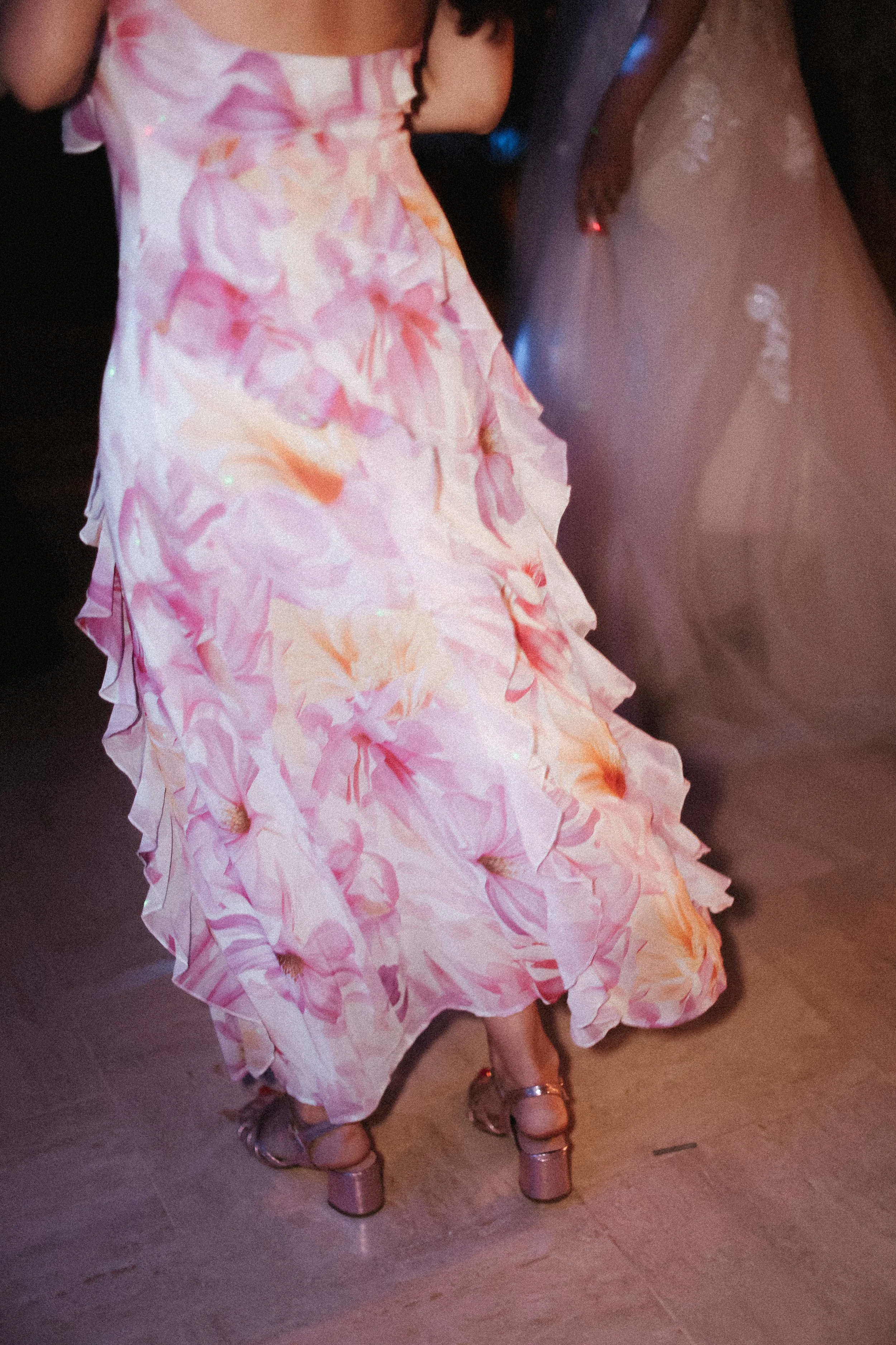 Femme portant une robe de bal à fleurs rose et pastel, avec des talons à plateforme rose, lors d'une occasion formelle ou fête.