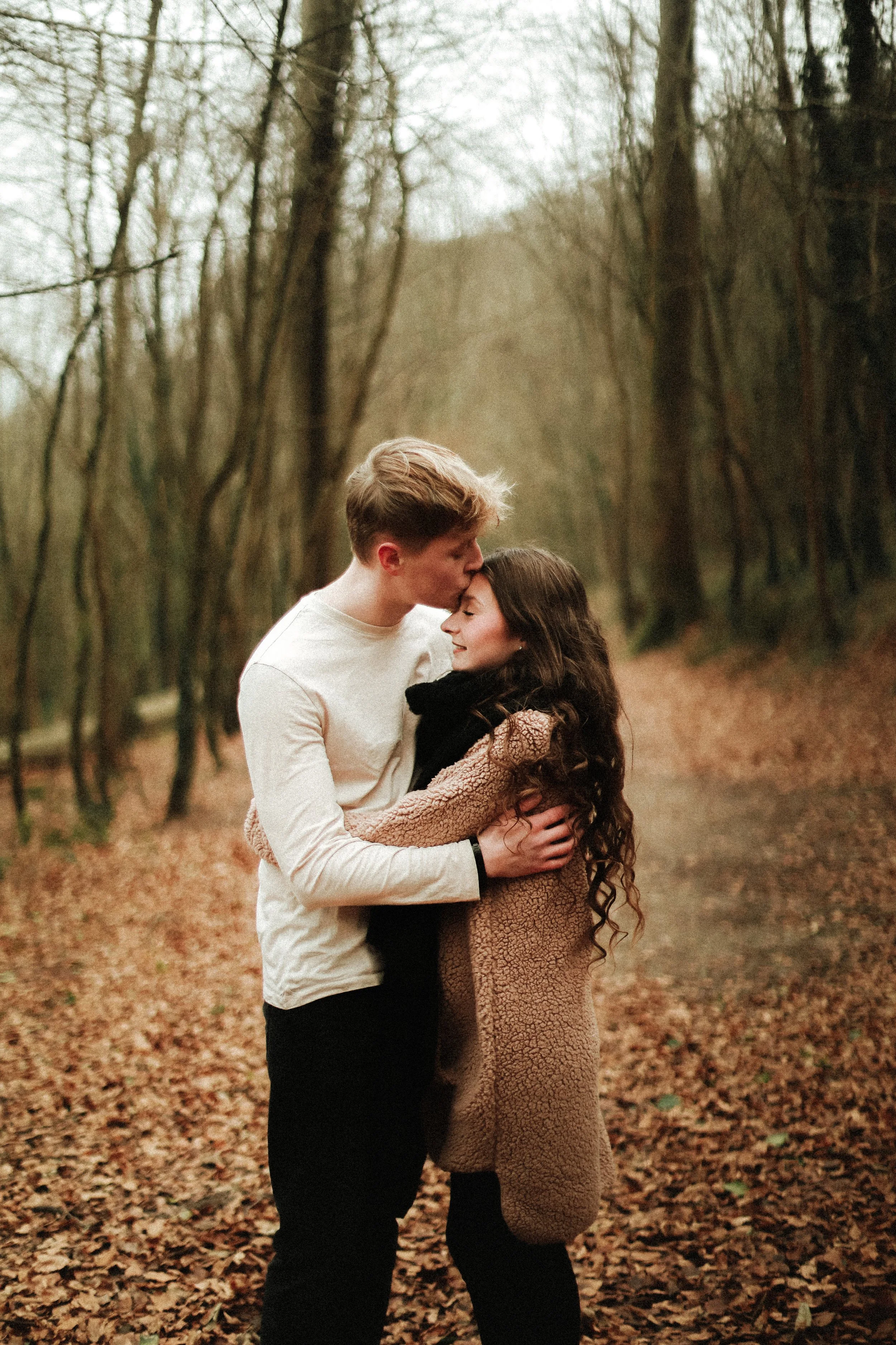 Un couple dans une forêt automnale s'embrassant tendrement.
