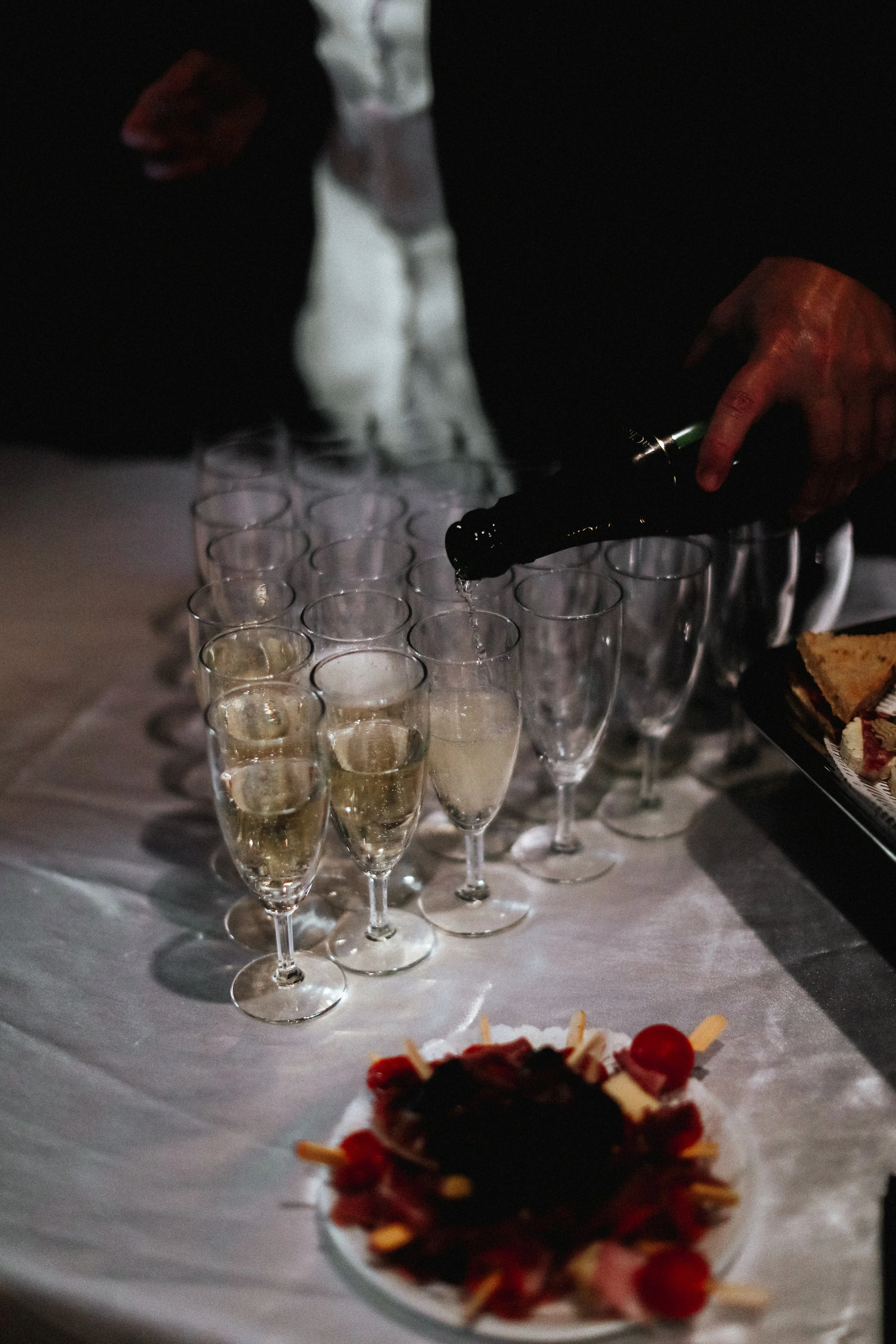 Une personne verse du champagne dans des flûtes, avec un gâteau décoratif sur la table.