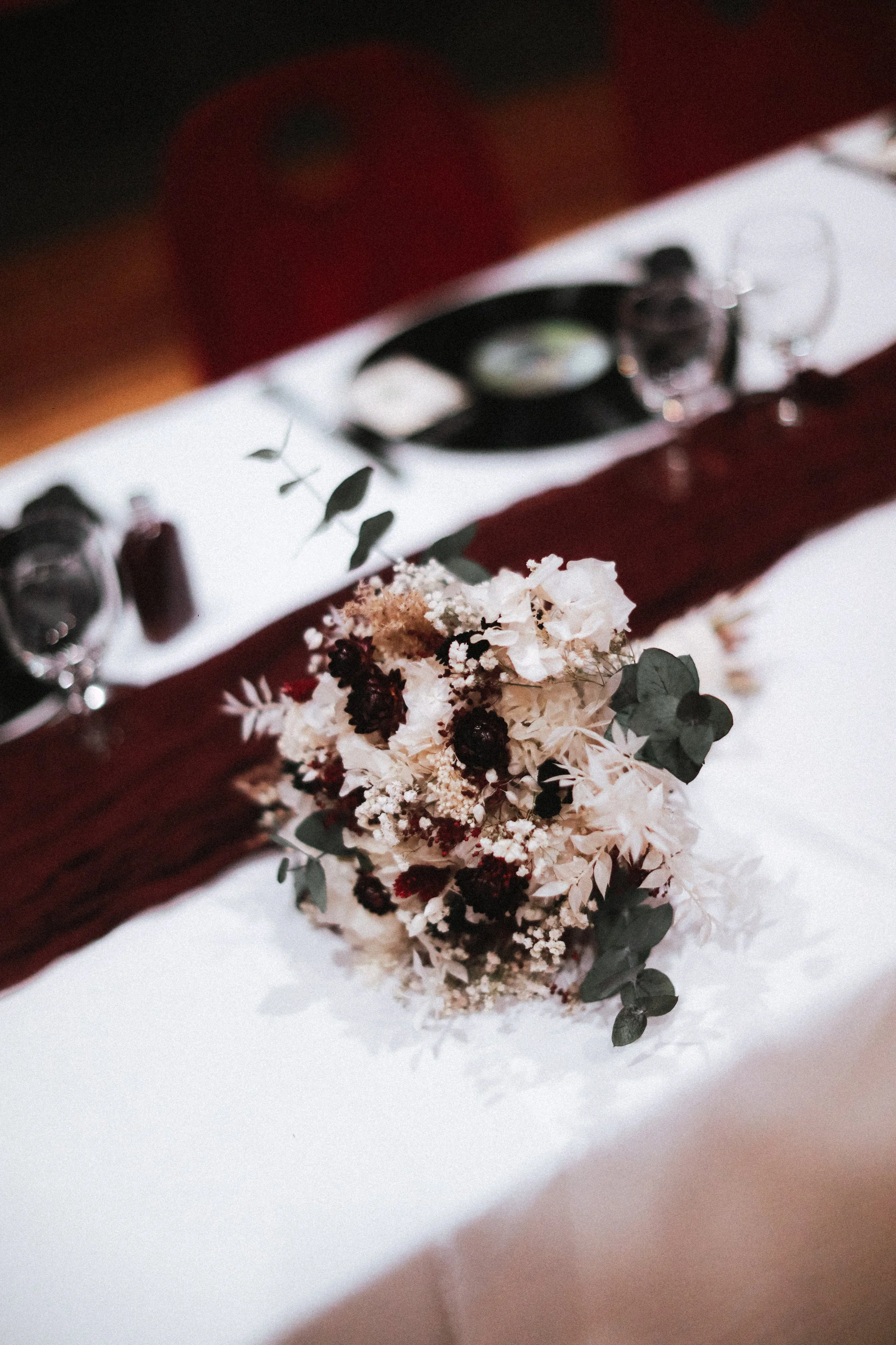Un arrangement floral sur une table de mariage avec une nappe blanche et une bande de velours rouge.