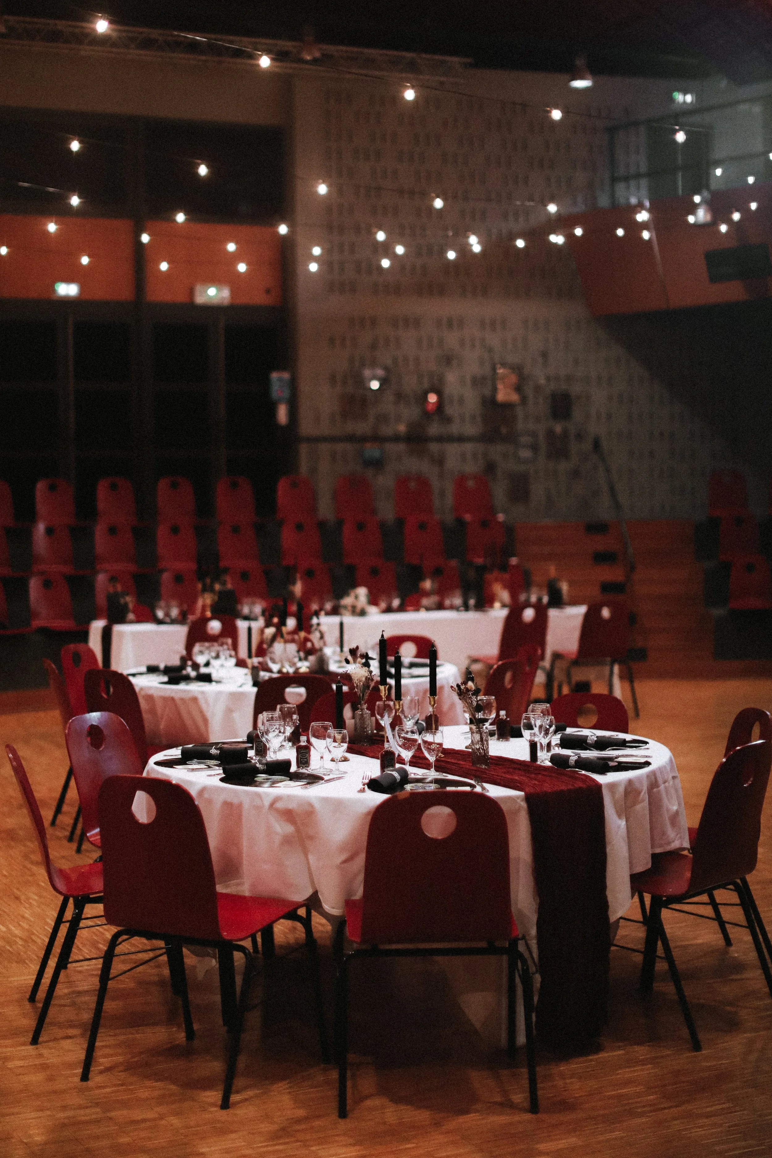 Salle de banquet élégante avec tables rondes, nappes blanches, décorations de bougies et fleurs, dans un environnement moderne avec des chaises rouges.