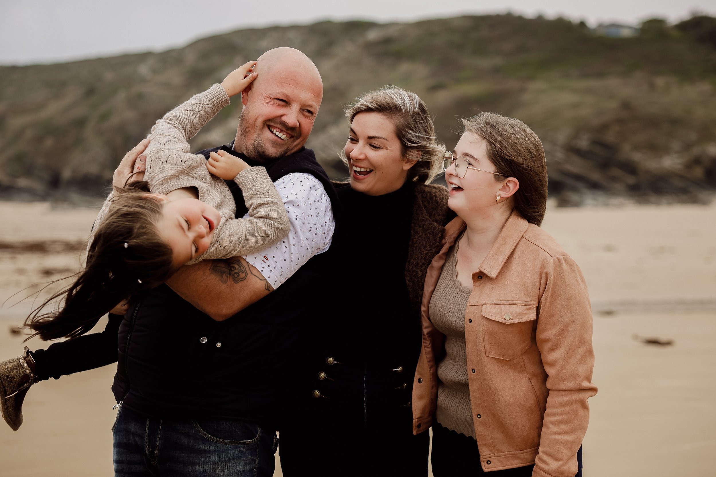 Une famille souriante en vacances à la plage, composée d'un homme, d'une femme, d'une fille et d'une jeune fille, profitant du soleil et de la nature.