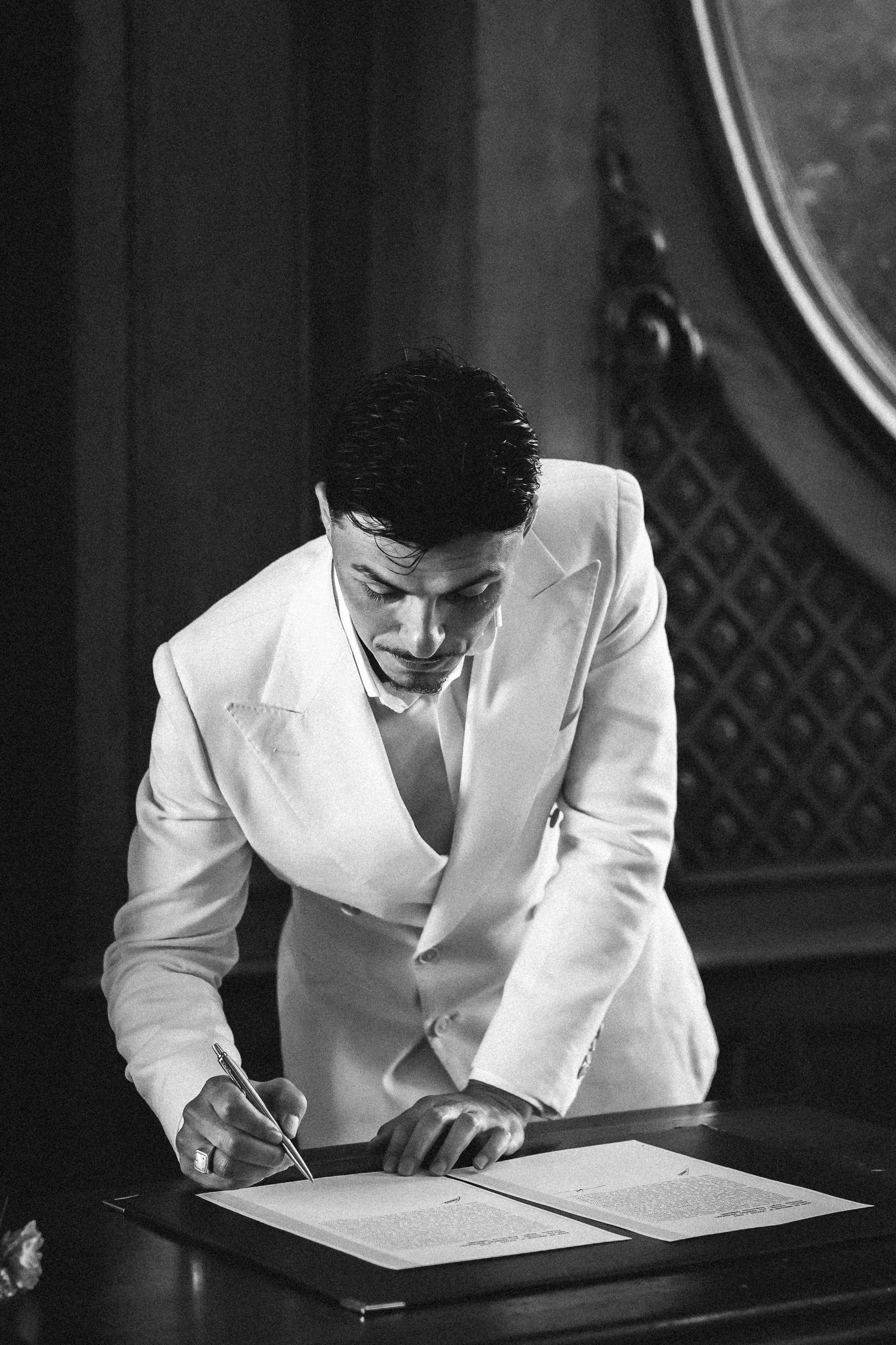 Homme en costume blanc signant un document sur une table