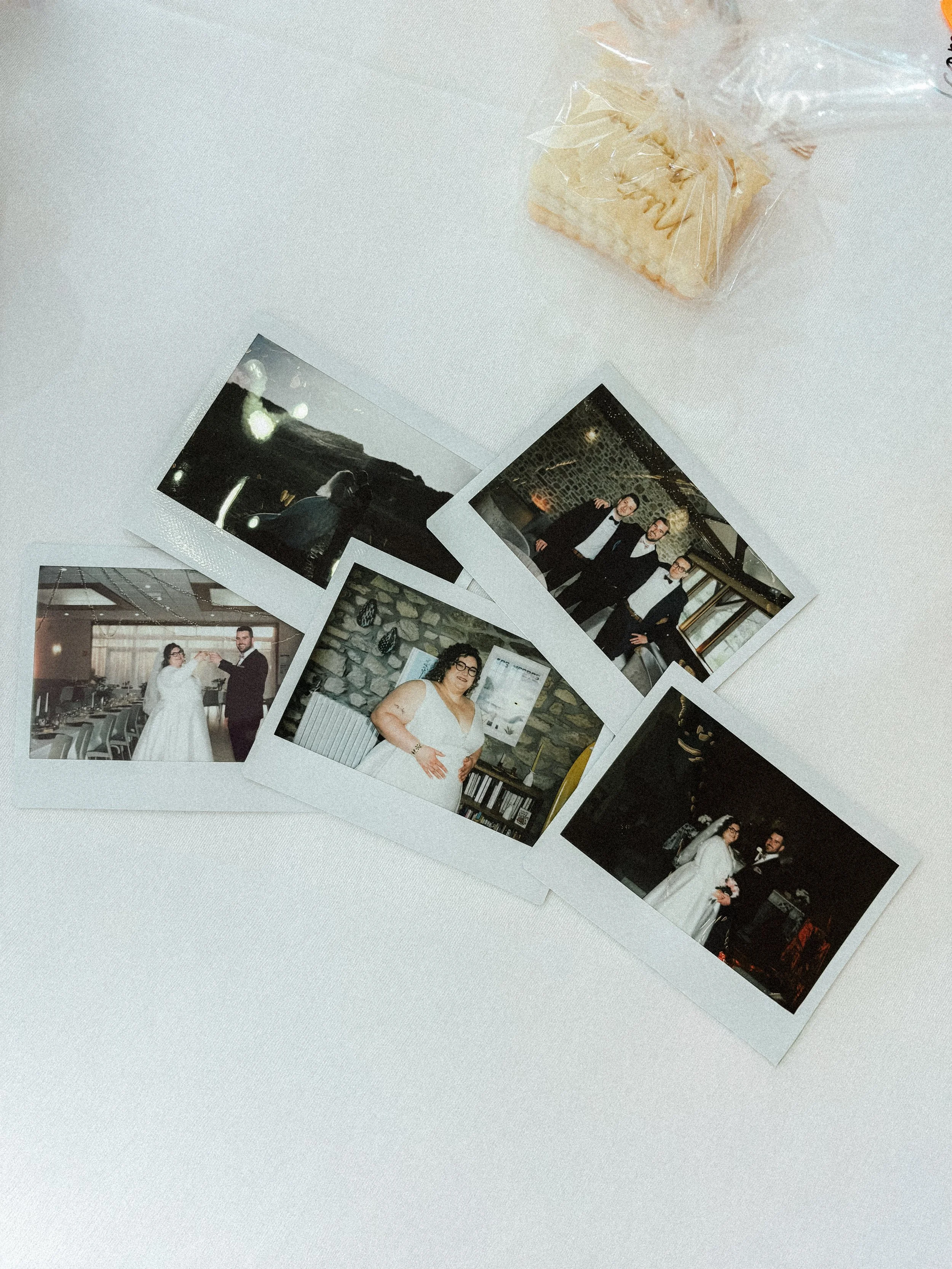 Photographies de plusieurs personnes lors d'une célébration, probablement un mariage, sur une table blanche avec un petit paquet de biscuits.