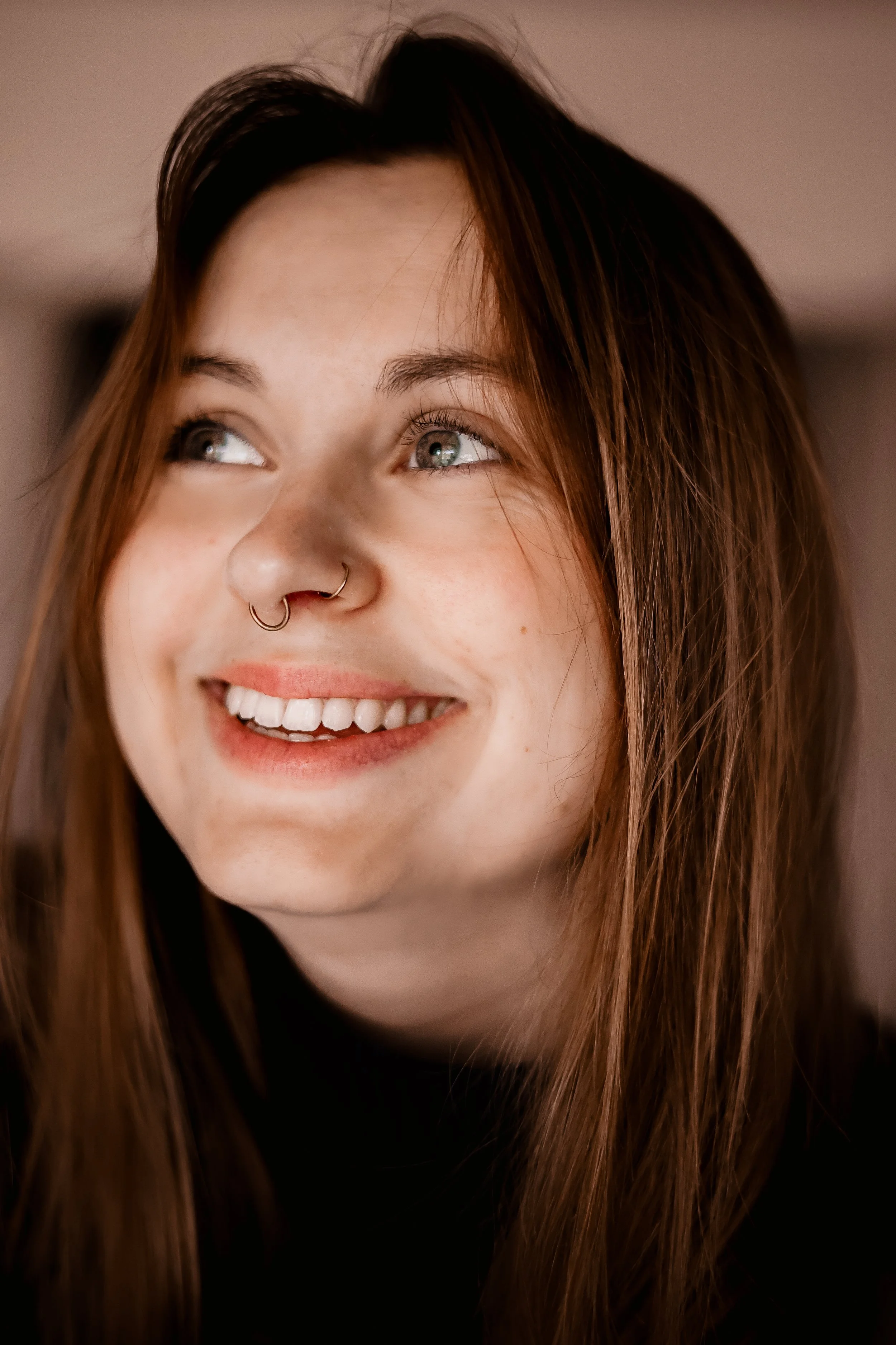 Jeune femme aux cheveux bruns, souriant, portant un piercing au nez, look naturel, dans un intérieur