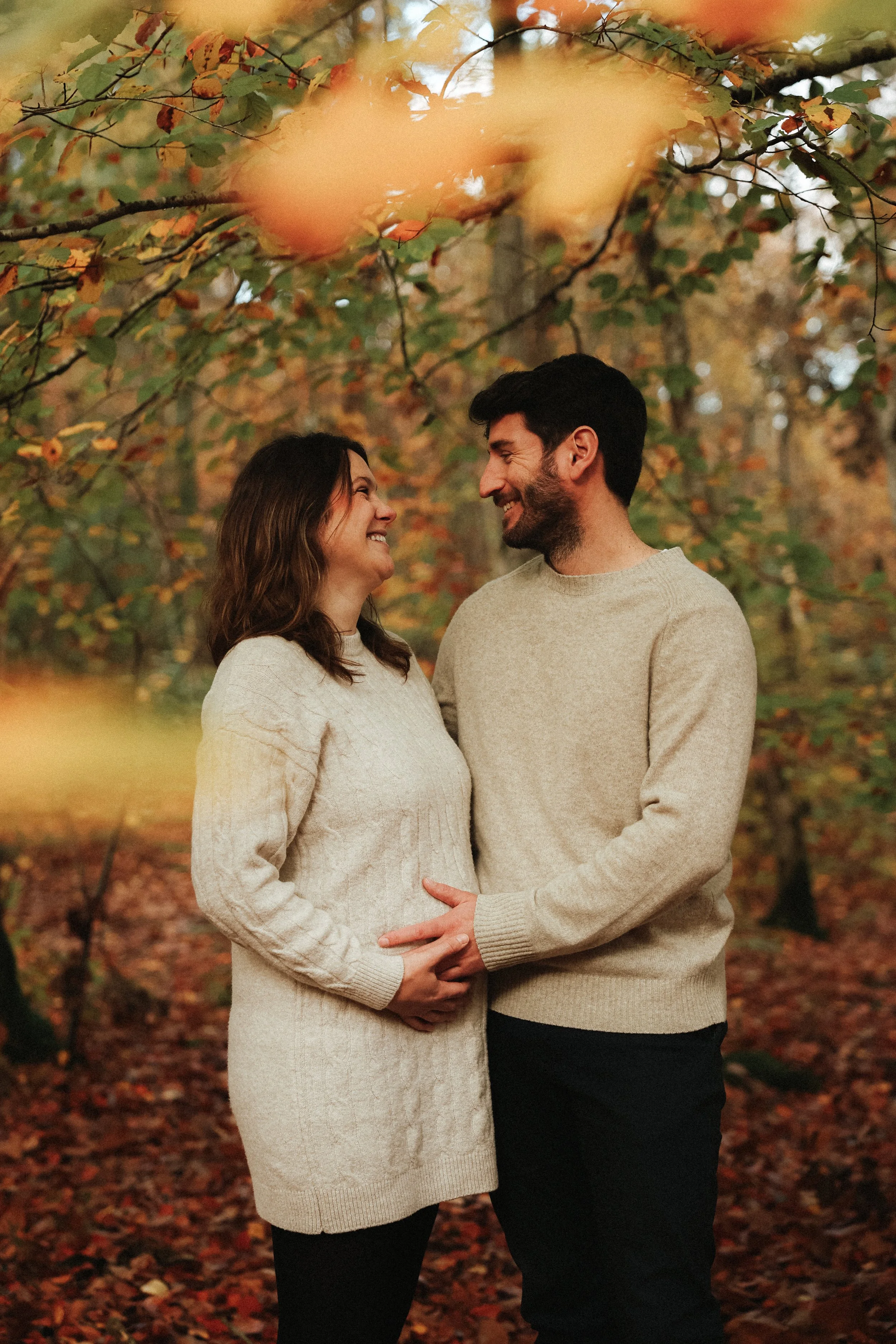Un couple en vêtements d'automne, amoureux, souriant et se tenant la main dans un bois aux couleurs automnales, feuilles orange, jaune et rouge.