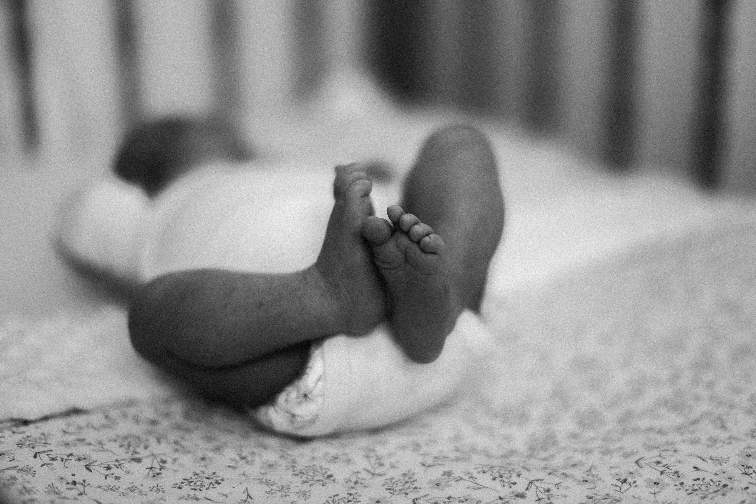 Un bébé nu couché sur le dos, vu de dos, sur un lit à motifs floraux, avec les jambes croisées.