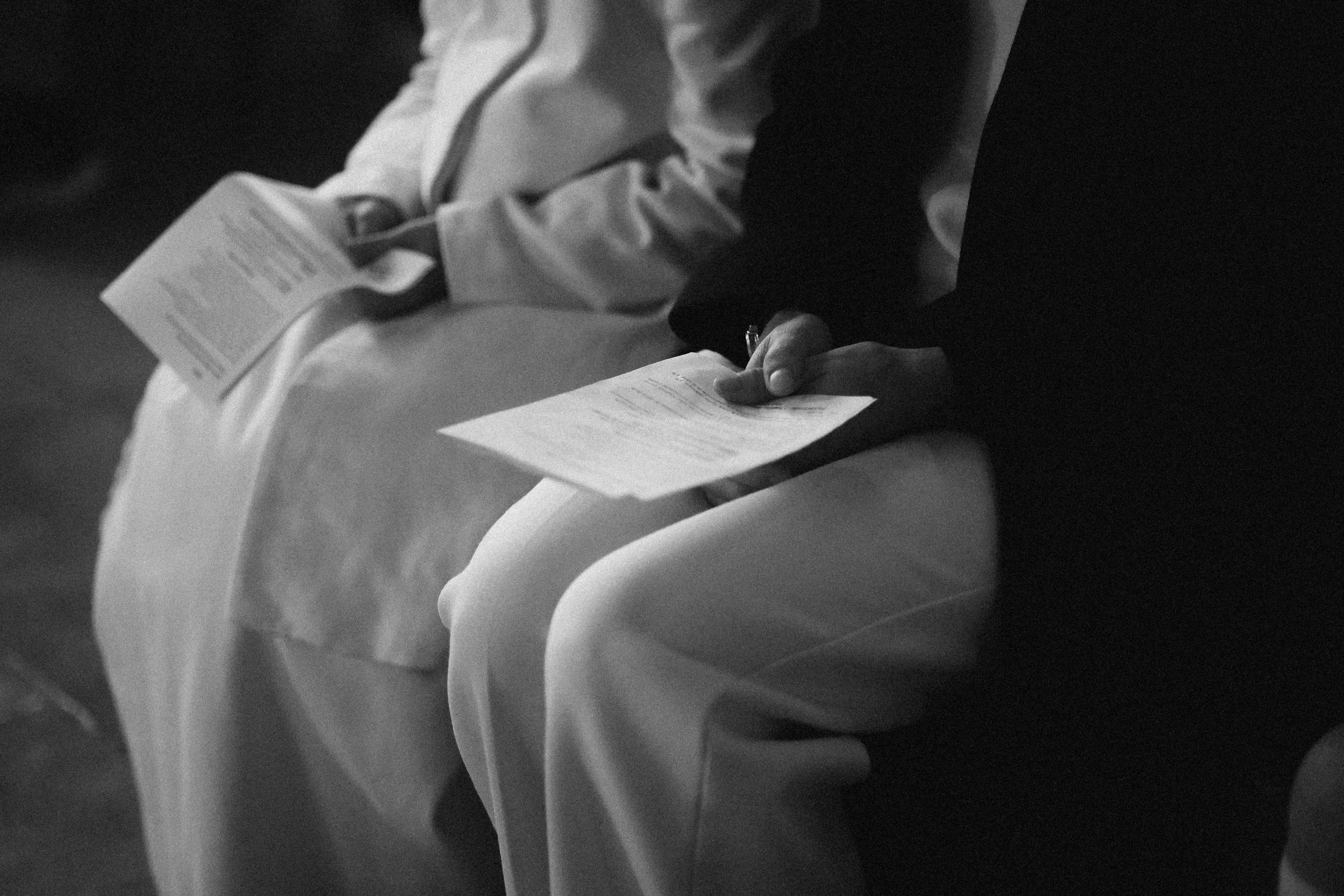 Deux personnes assises à une conférence ou un évènement, tenant des brochures ou des programmes.