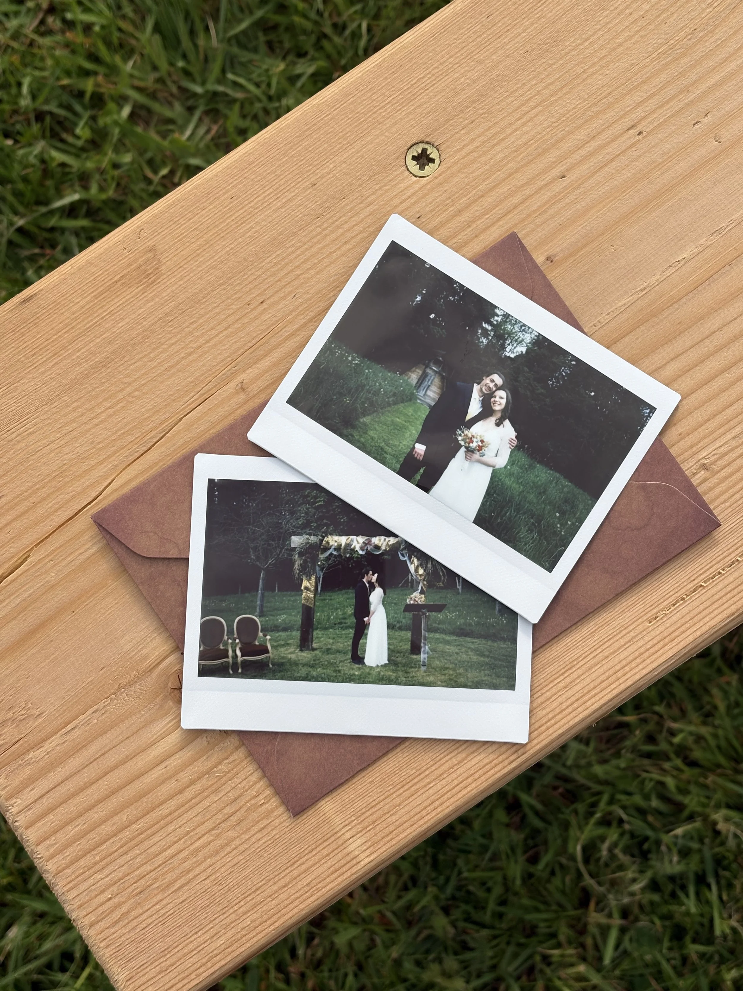 Deux photographies de mariage sur une table en bois, avec un fond de pelouse verte.