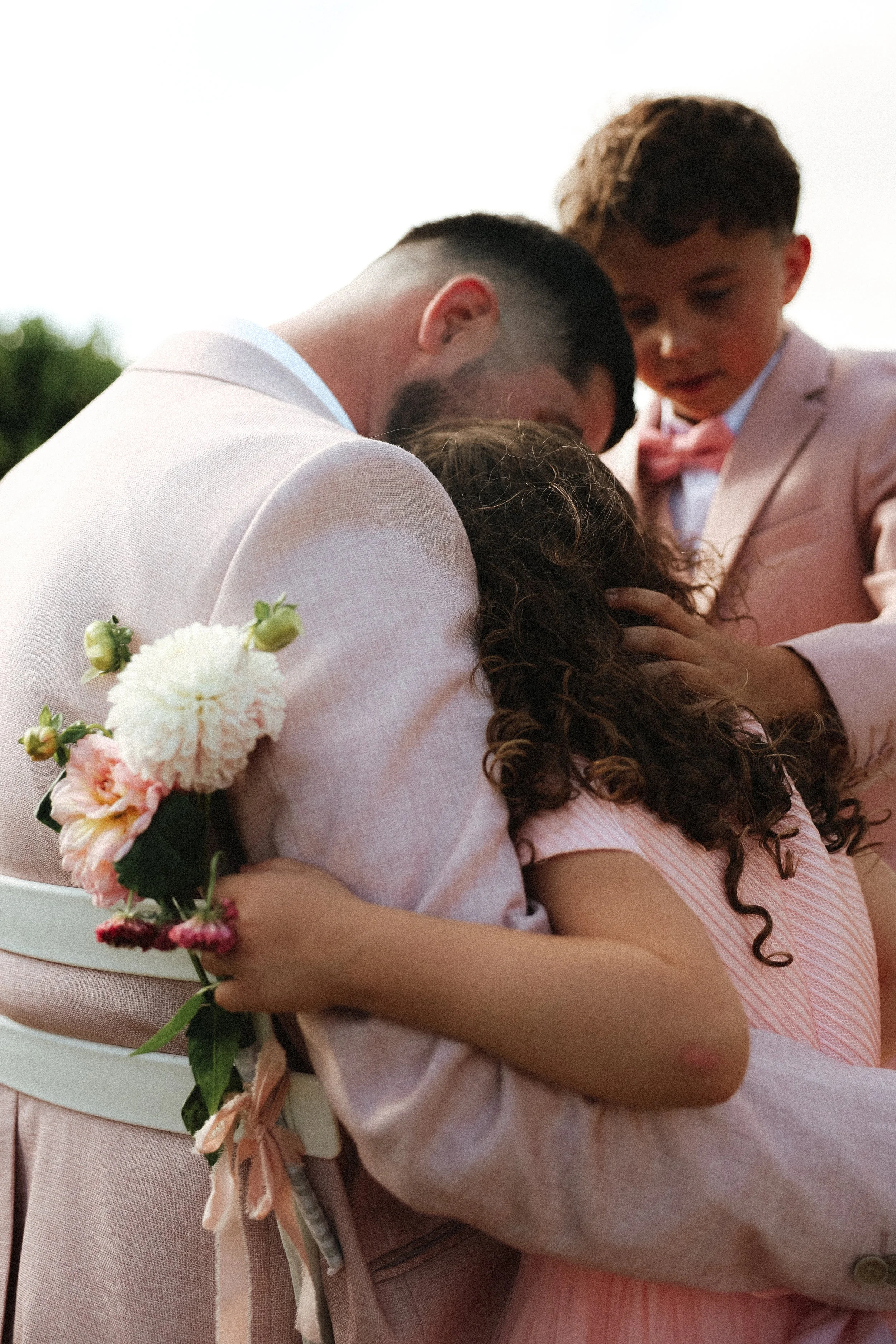 Un groupe de personnes en train de s'étreindre lors d'une cérémonie, avec des fleurs en arrière-plan.
