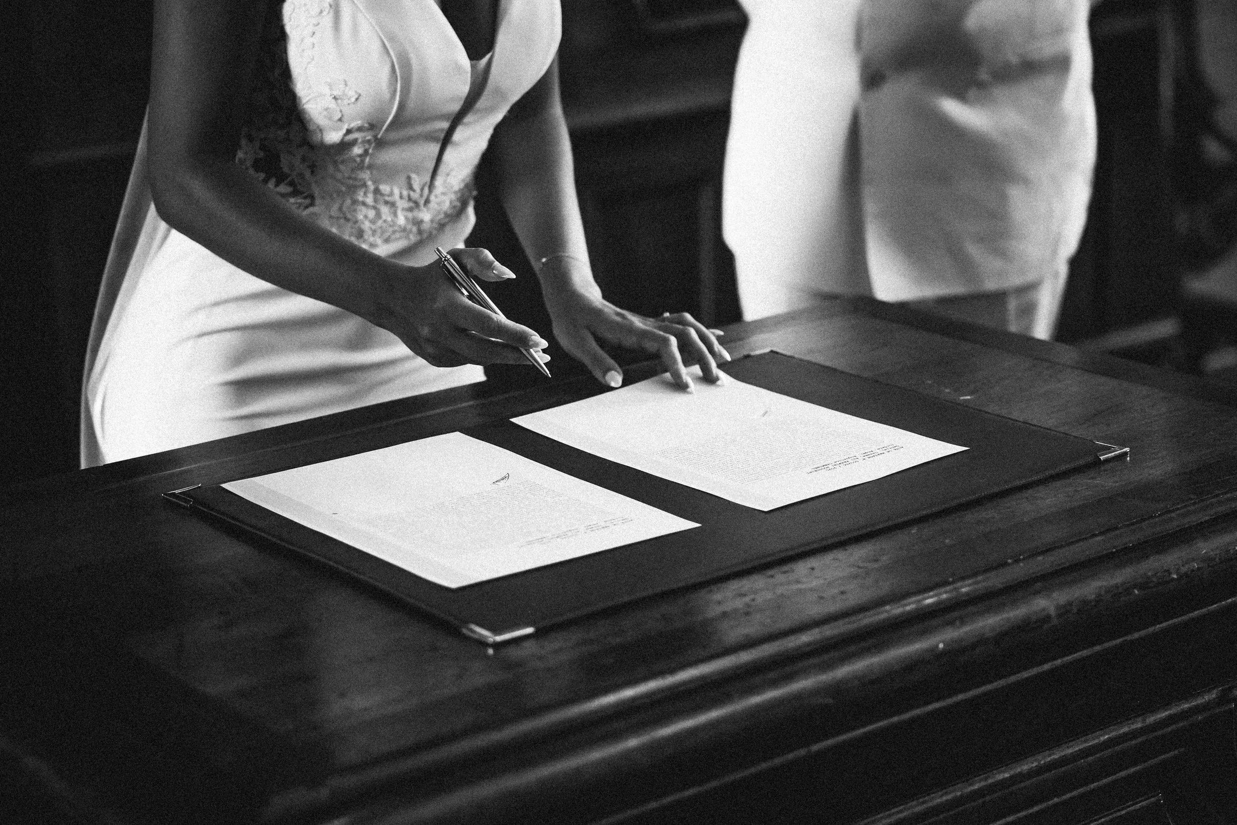Une femme écrit sur une feuille posée sur une table en bois, en noir et blanc.