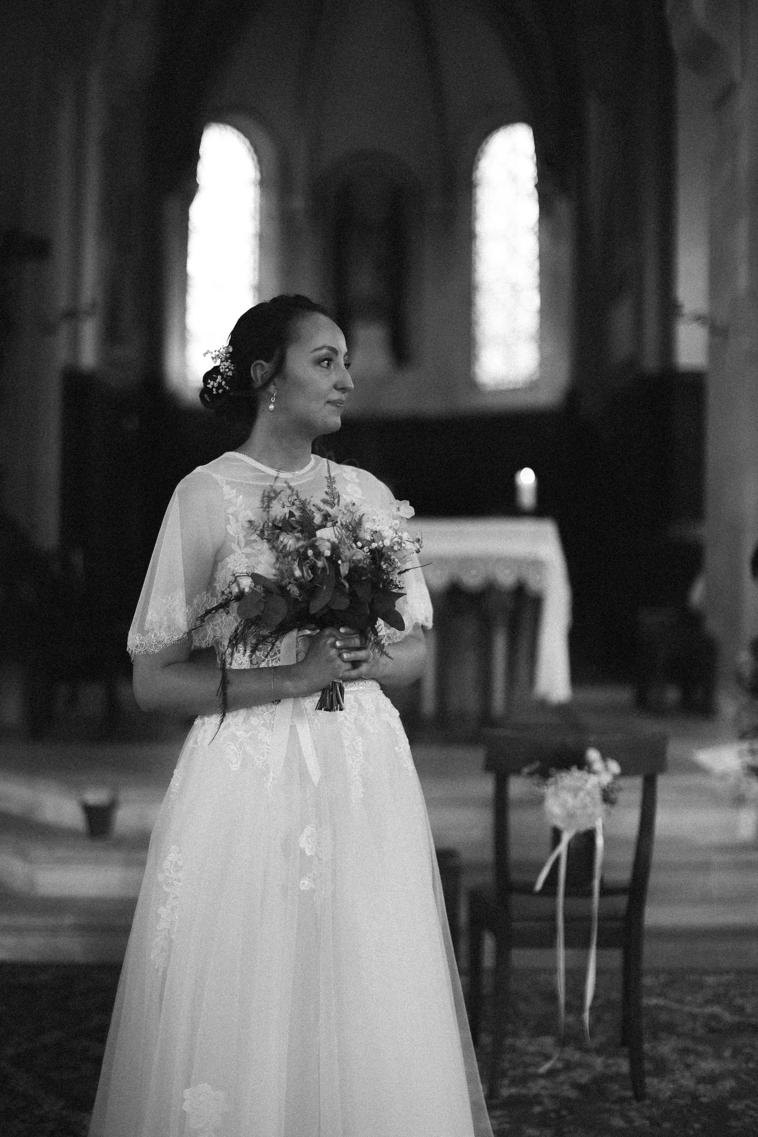 Une femme en robe de mariage blanche tient un bouquet de fleurs dans une église.