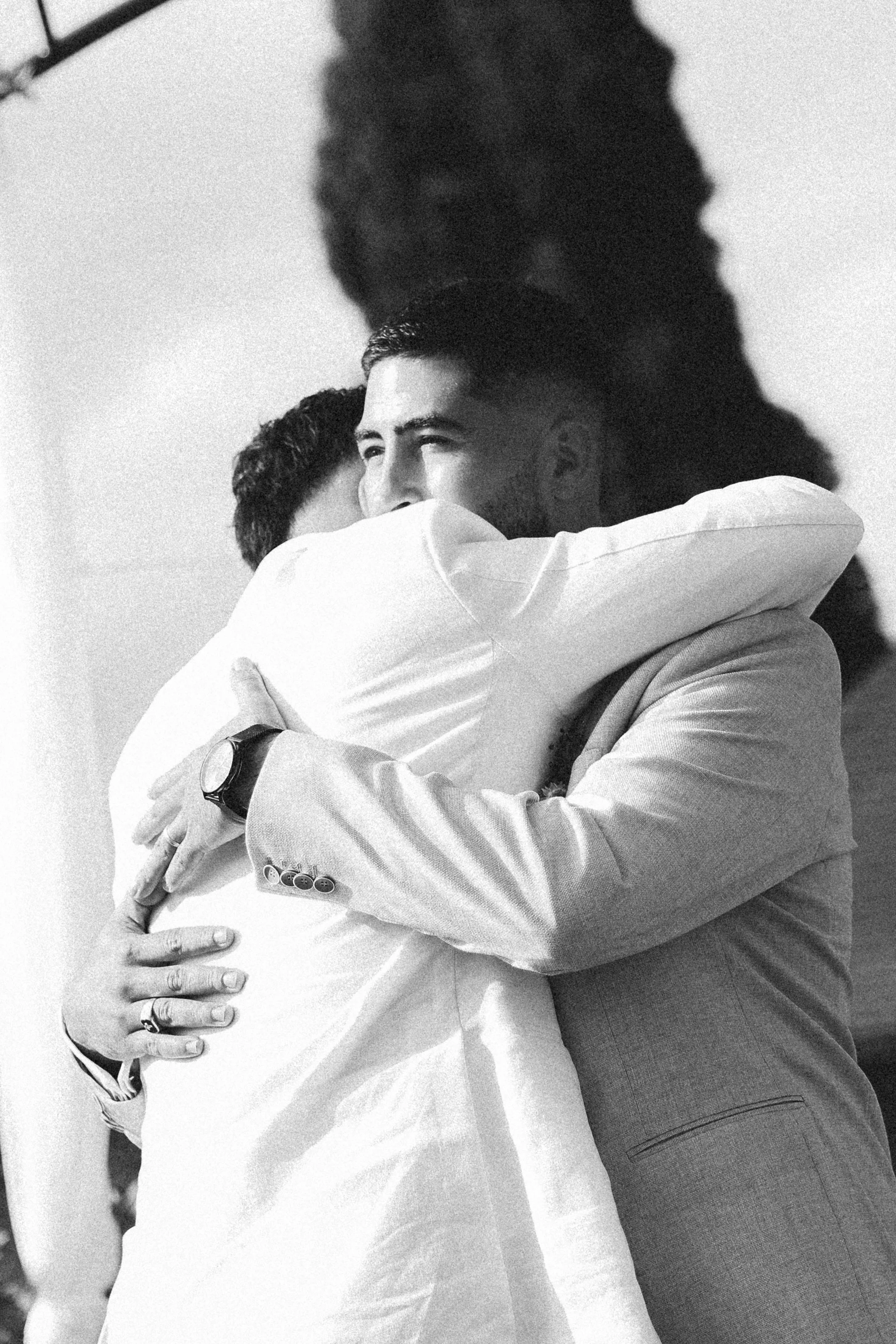 Deux hommes s'embrassent en étreinte affectueuse, en tenue formelle, dans un format noir et blanc.