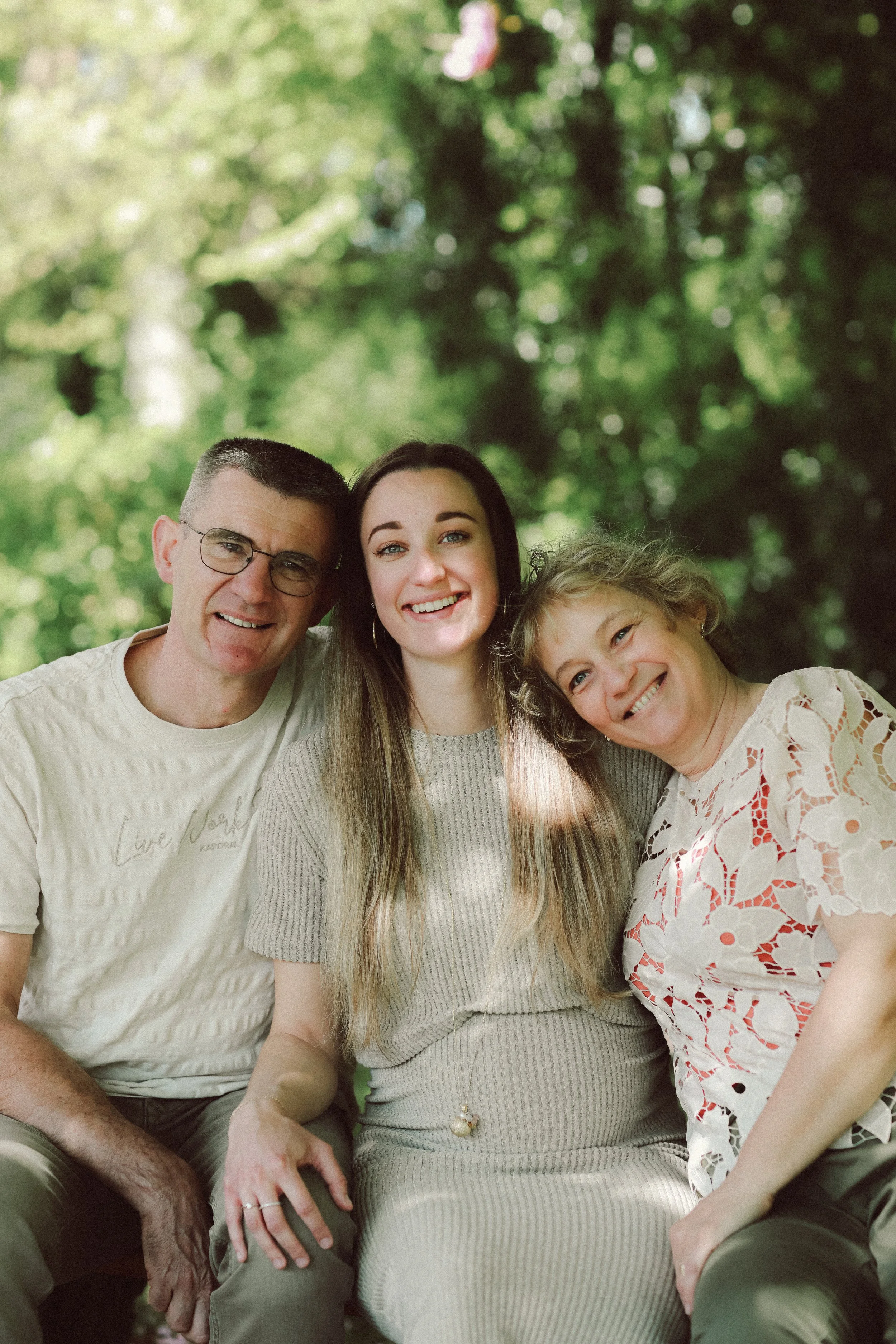 Trois personnes souriantes assises à l'extérieur avec un fond d'arbres verts.