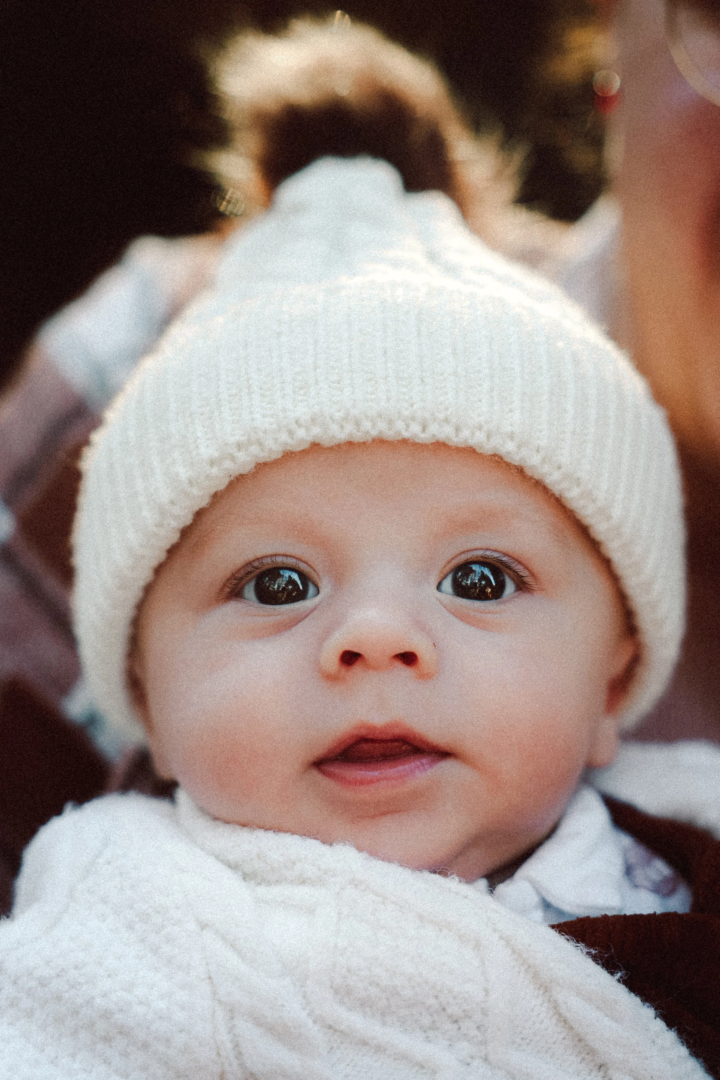 Un bébé yeux grands ouverts, portant un bonnet blanc, regardant directement l'appareil photo.
