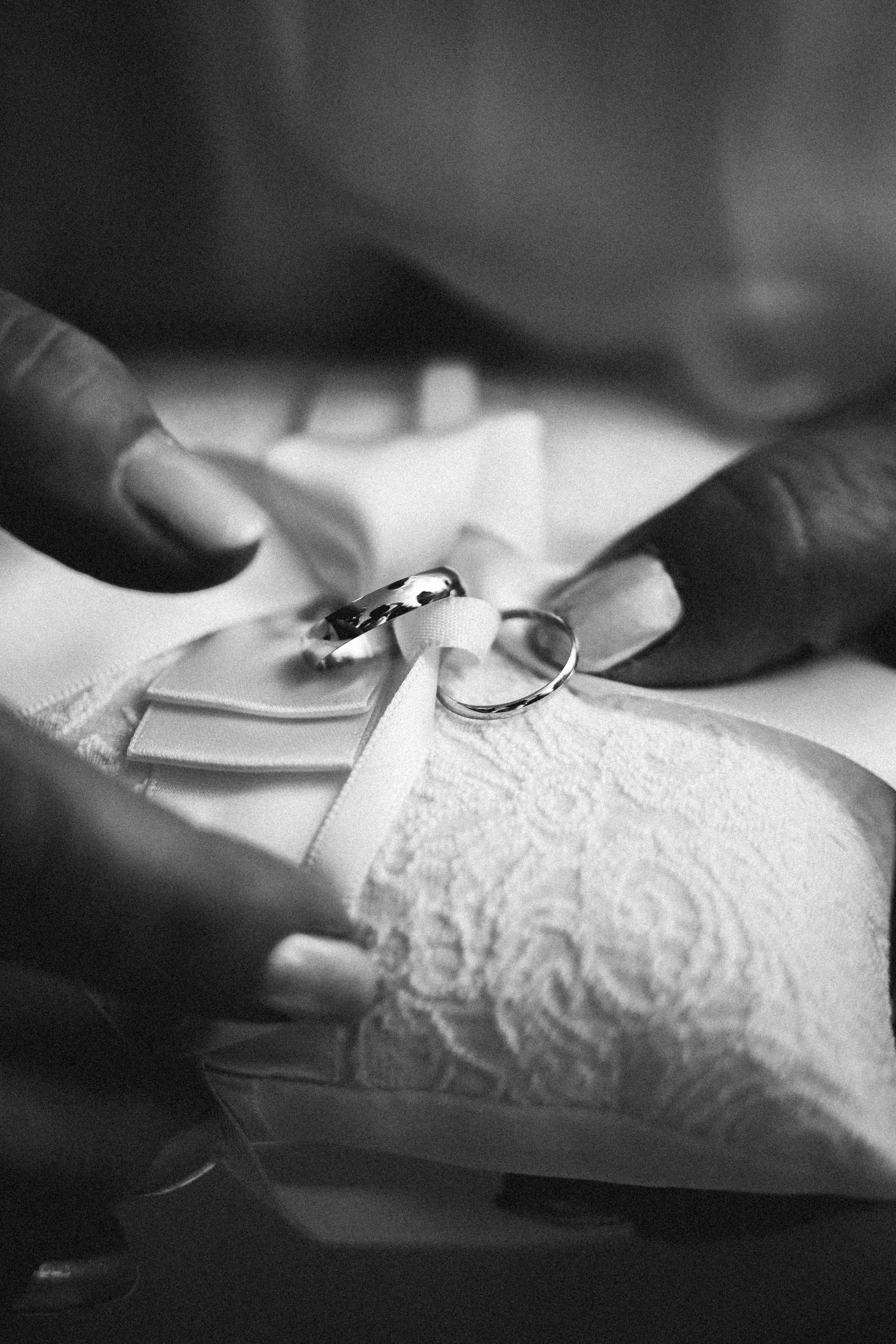 Anneau de mariage et alliance posés sur un coussin blanc en tissu brodé, tenu par deux mains.