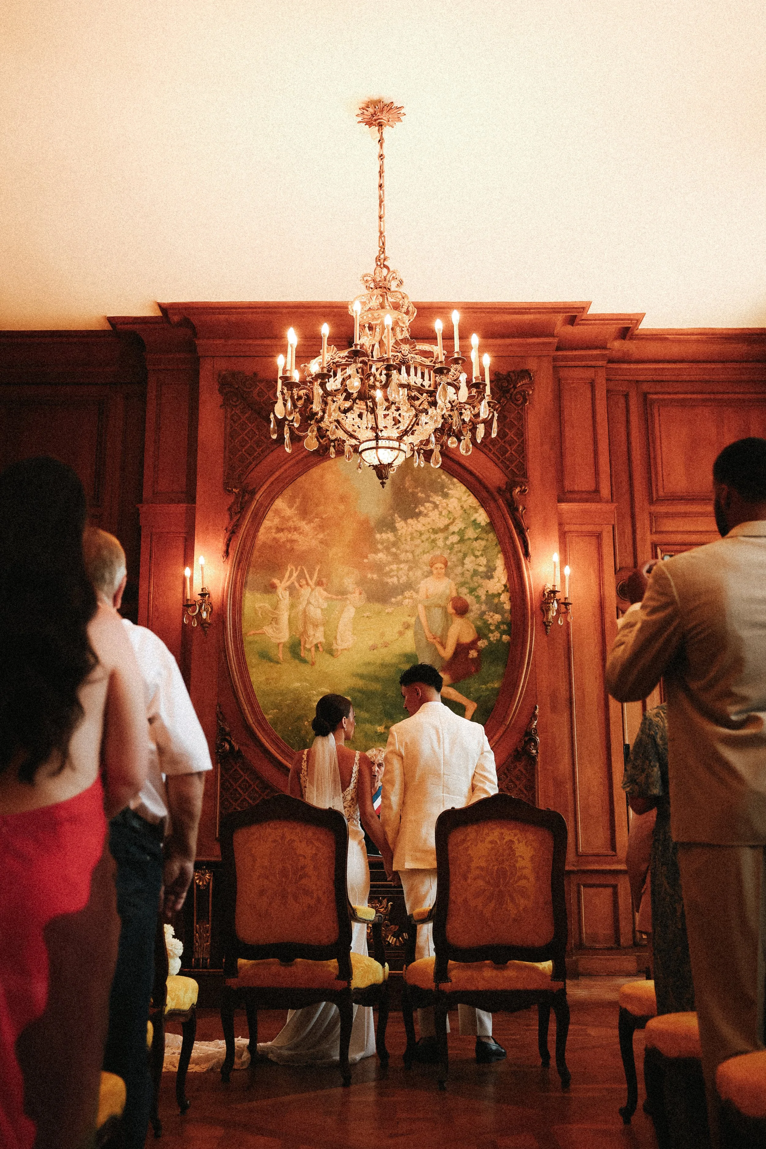 Un couple se mariant devant un tableau dans une salle ornée en bois avec un lustre chandelier