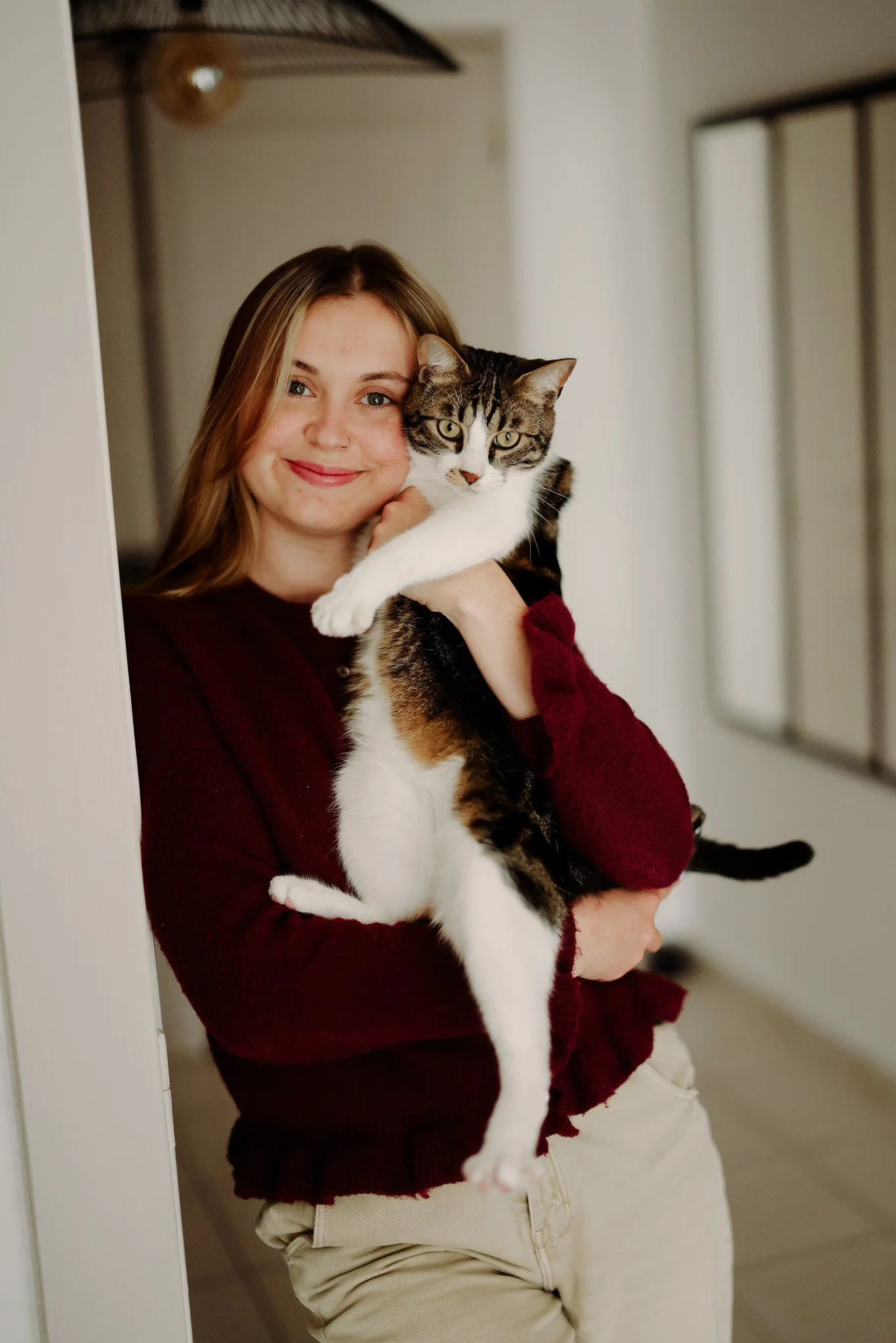 Une femme souriante tenant un chat tigré avec un fond intérieur de maison.