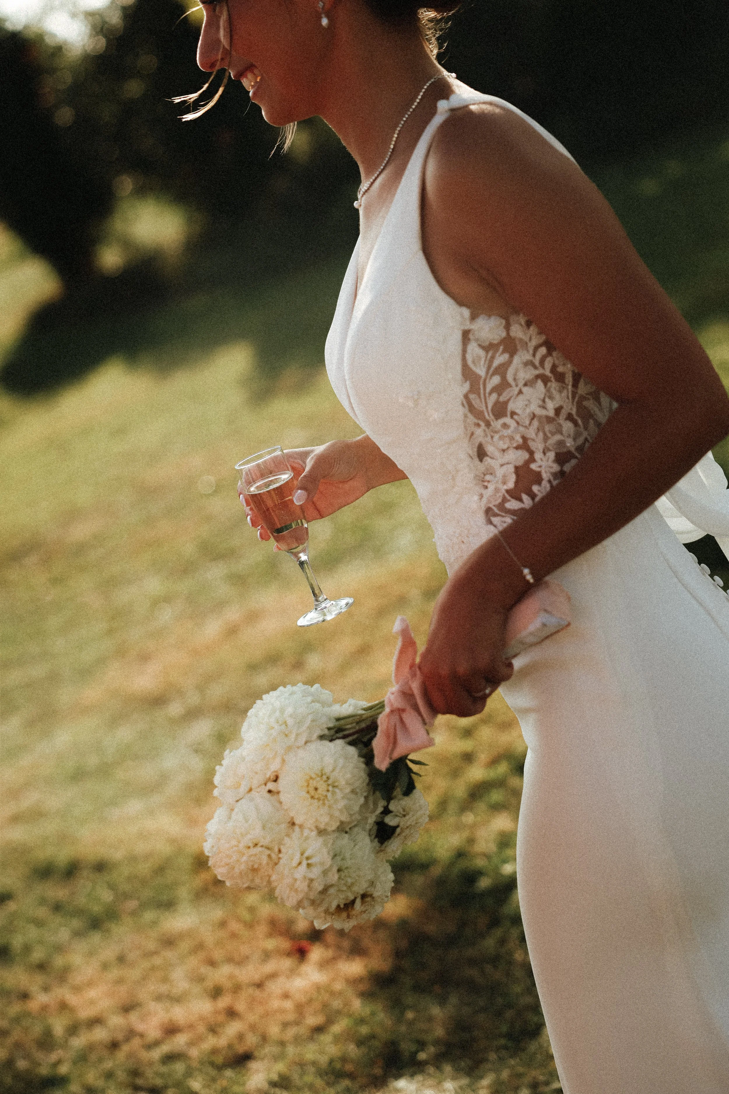 Une femme en robe de mariage tenant un bouquet de fleurs blanches et un verre de champagne dans un cadre extérieur