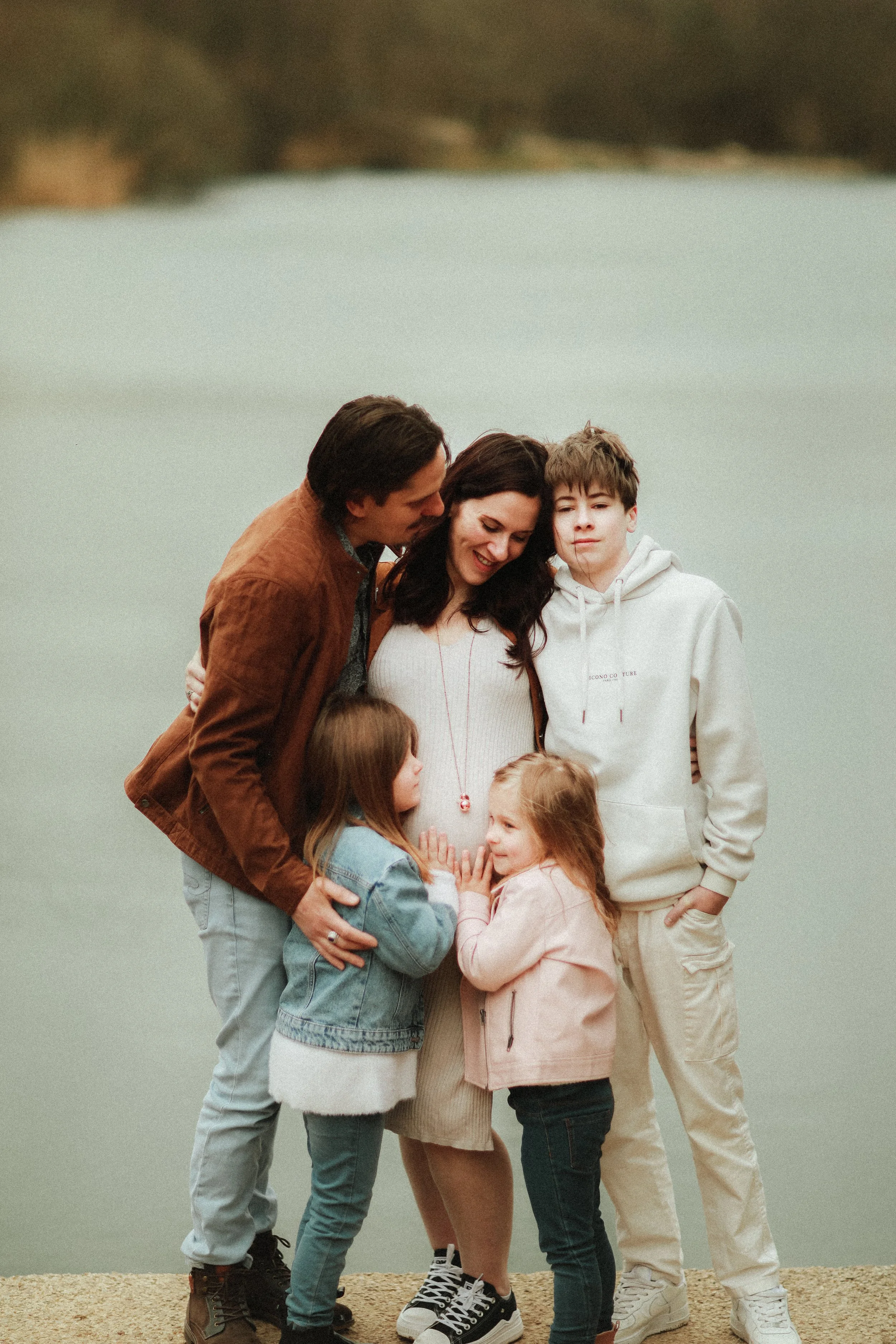 Une famille réunie près d'un lac, la mère enceinte est entourée par deux filles et deux garçons, tous souriants.