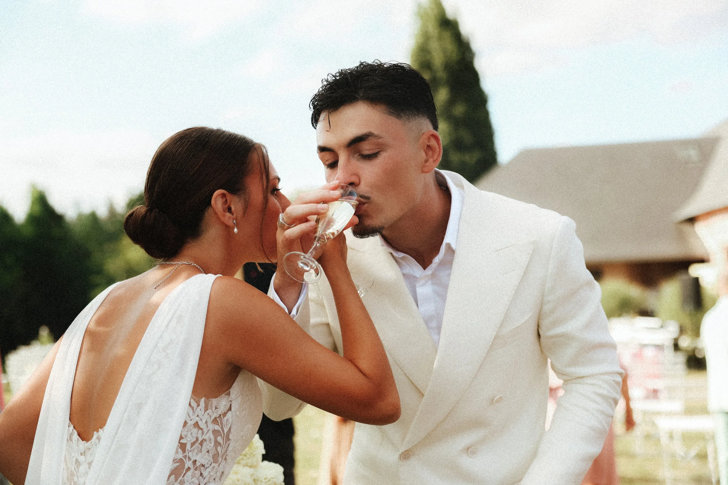 Un couple en tenue de mariage partage une coupe de champagne lors d'une célébration en plein air.