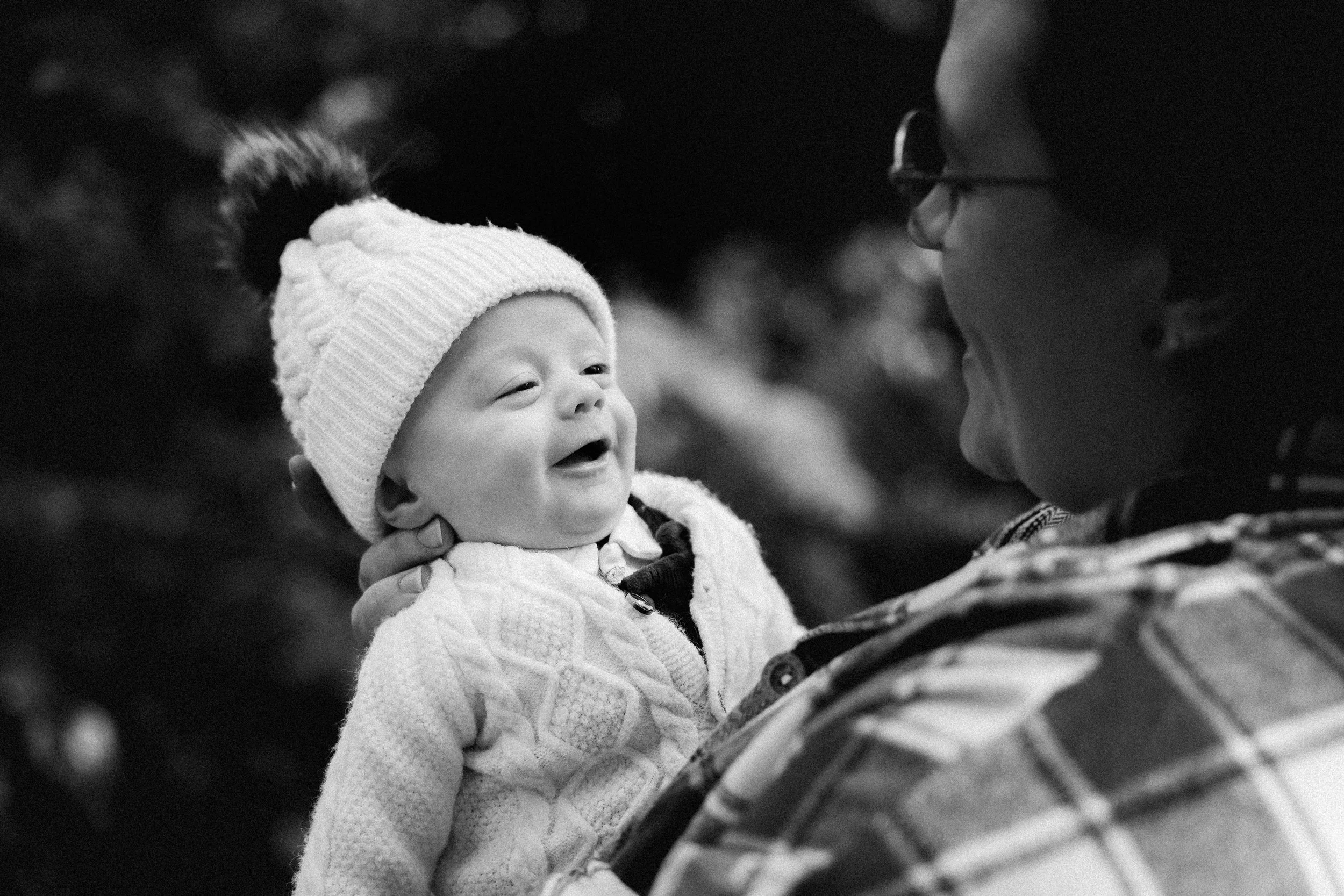 Un adulte tient un jeune enfant dans ses bras, tous deux souriants et puisant dans un moment de bonheur, en plein air.