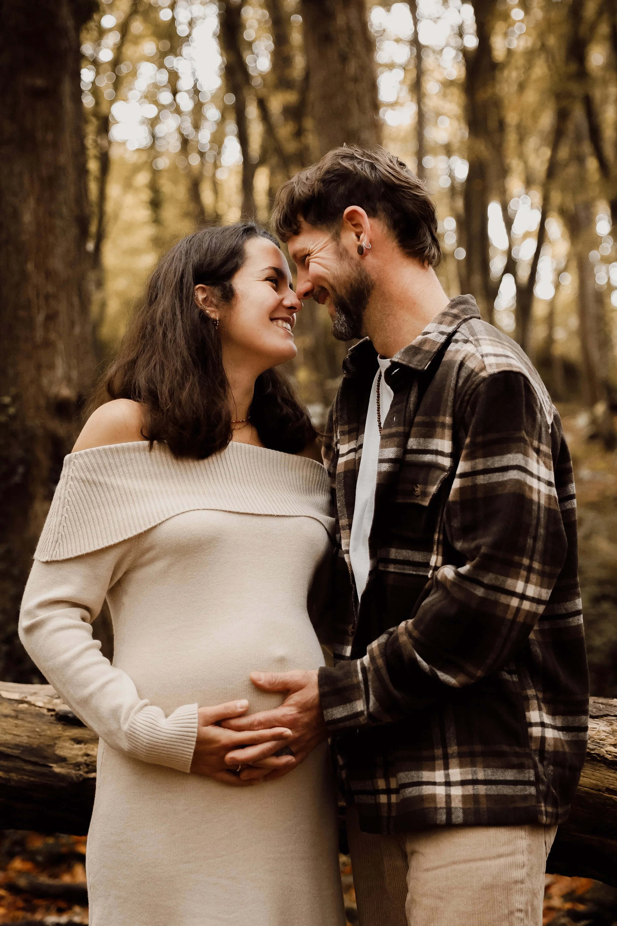 Un couple heureux, l'homme tenant le ventre de la femme enceinte, se tenant face à face dans une forêt pendant l'automne.