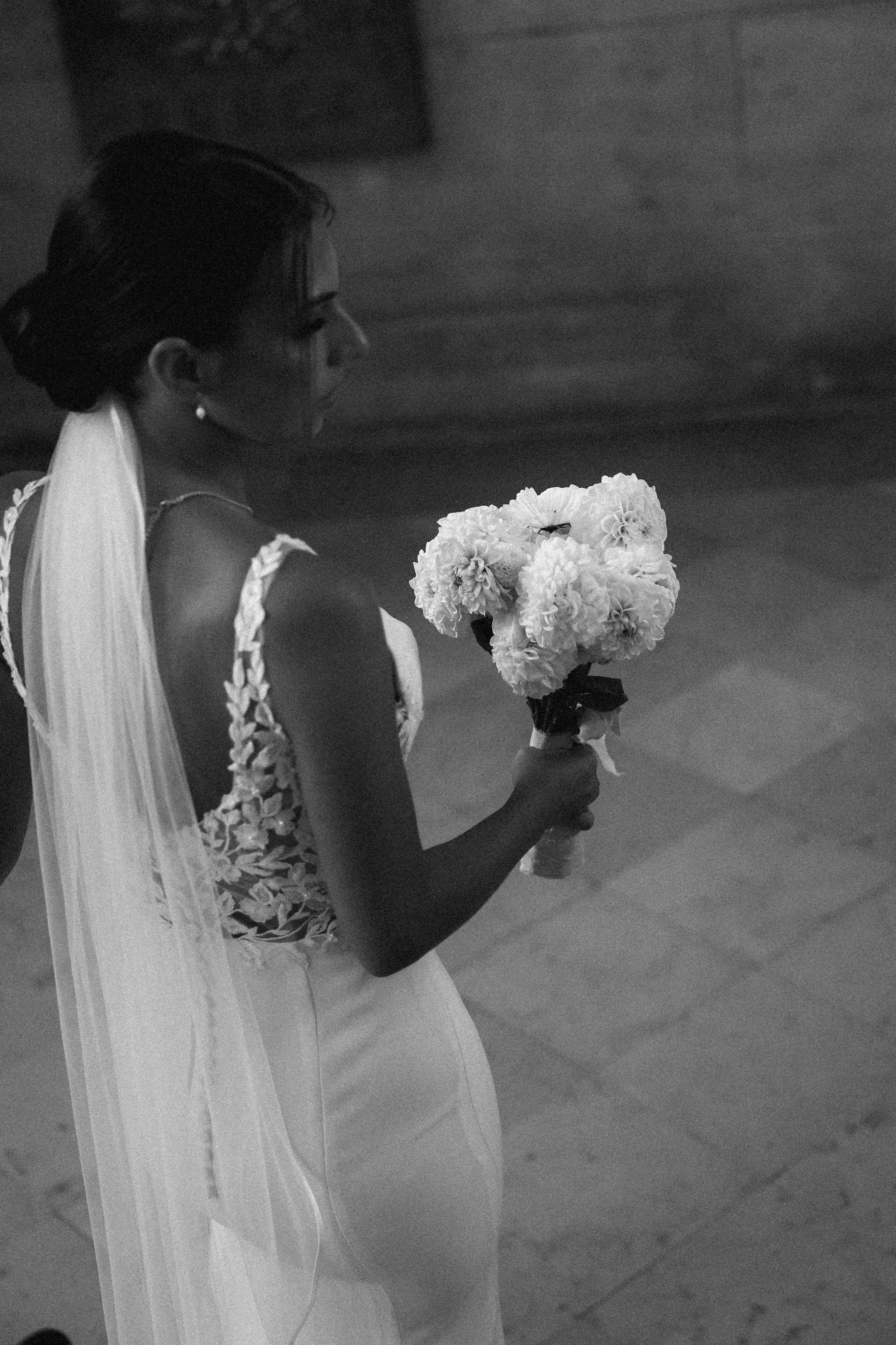 Une mariée en robe blanche avec un voile tient un bouquet de fleurs blanc.