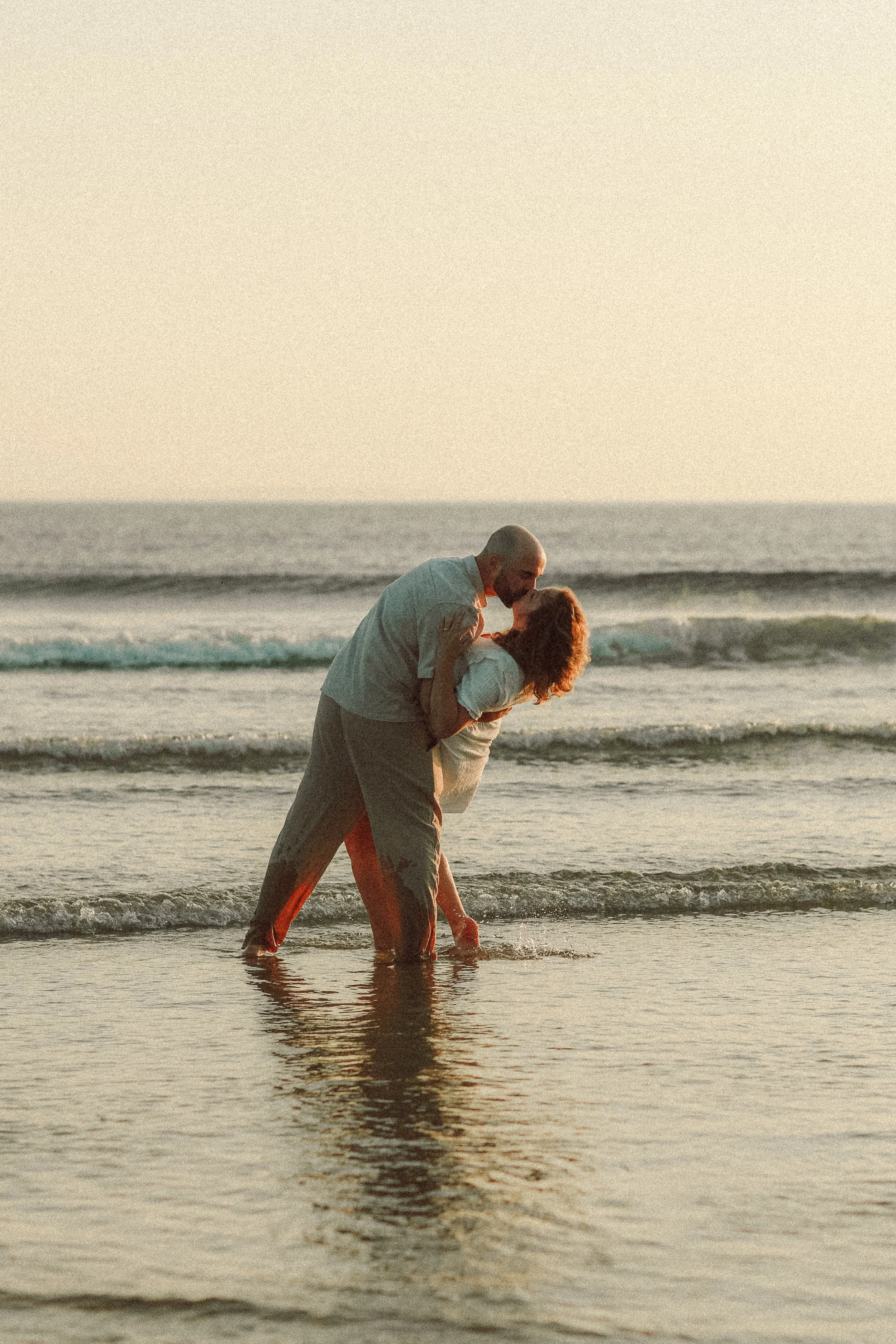 Un couple danse dans l'eau de la mer au coucher du soleil, s'enlaçant et partageant un moment romantique.