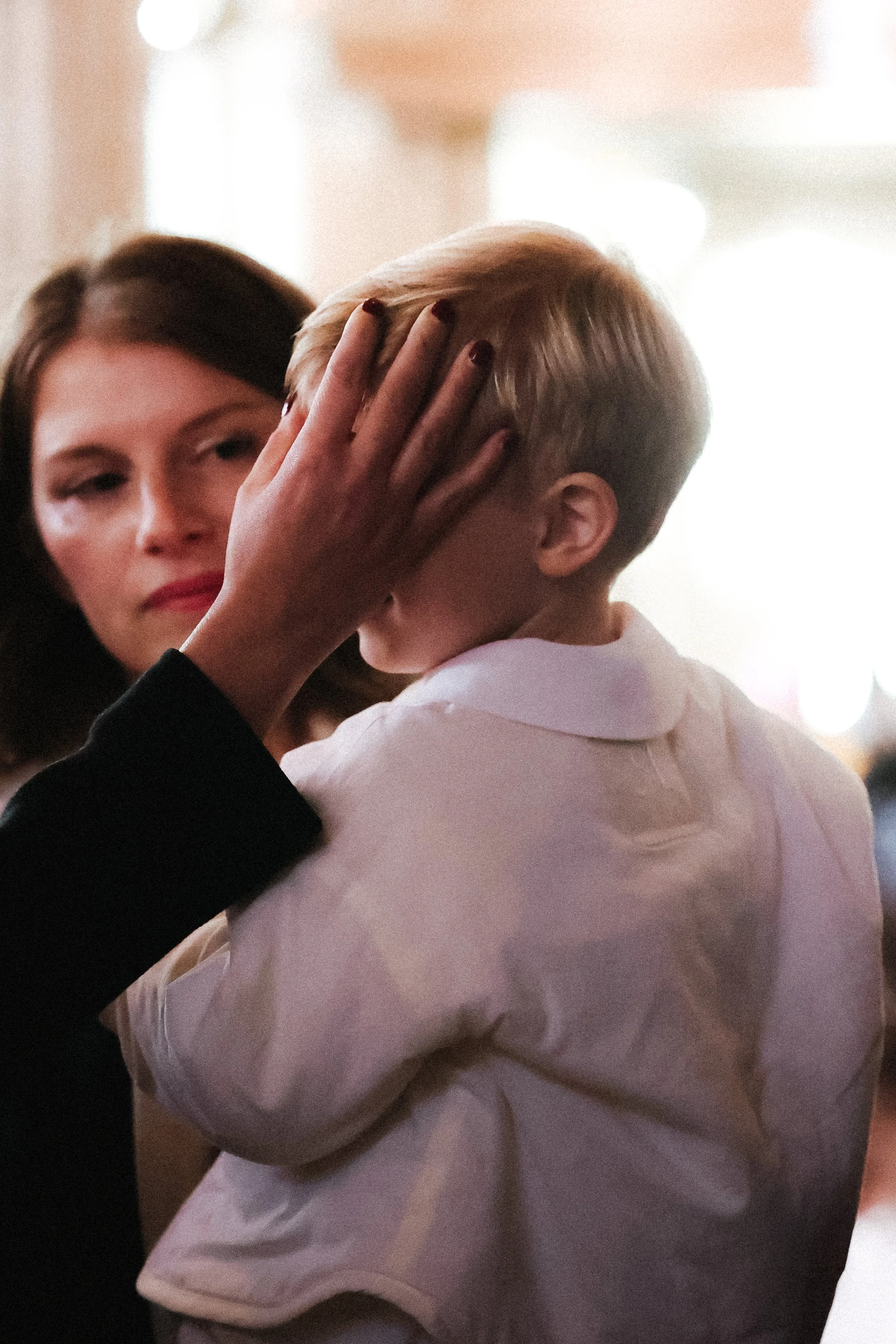 Une femme et un jeune garçon partagent un moment tendre. La femme tient la tête du garçon contre son visage, dans un geste d'affection ou de réconfort, dans un environnement intérieur chaleureux et flou.