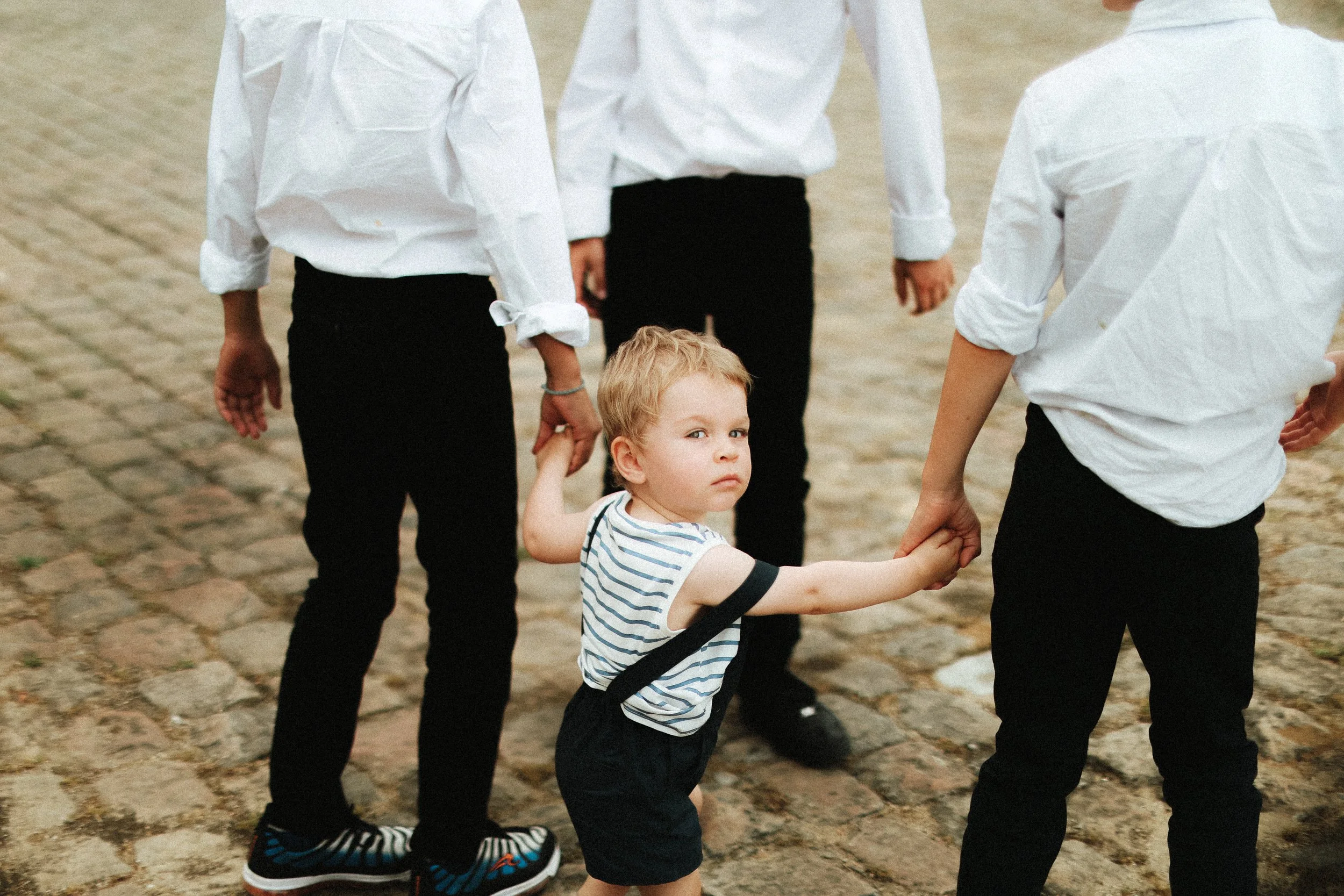 Un jeune enfant tenant la main d'une personne plus âgée dans une foule de personnes portant toutes des chemises blanches et des pantalons noirs, sur un sol pavé.