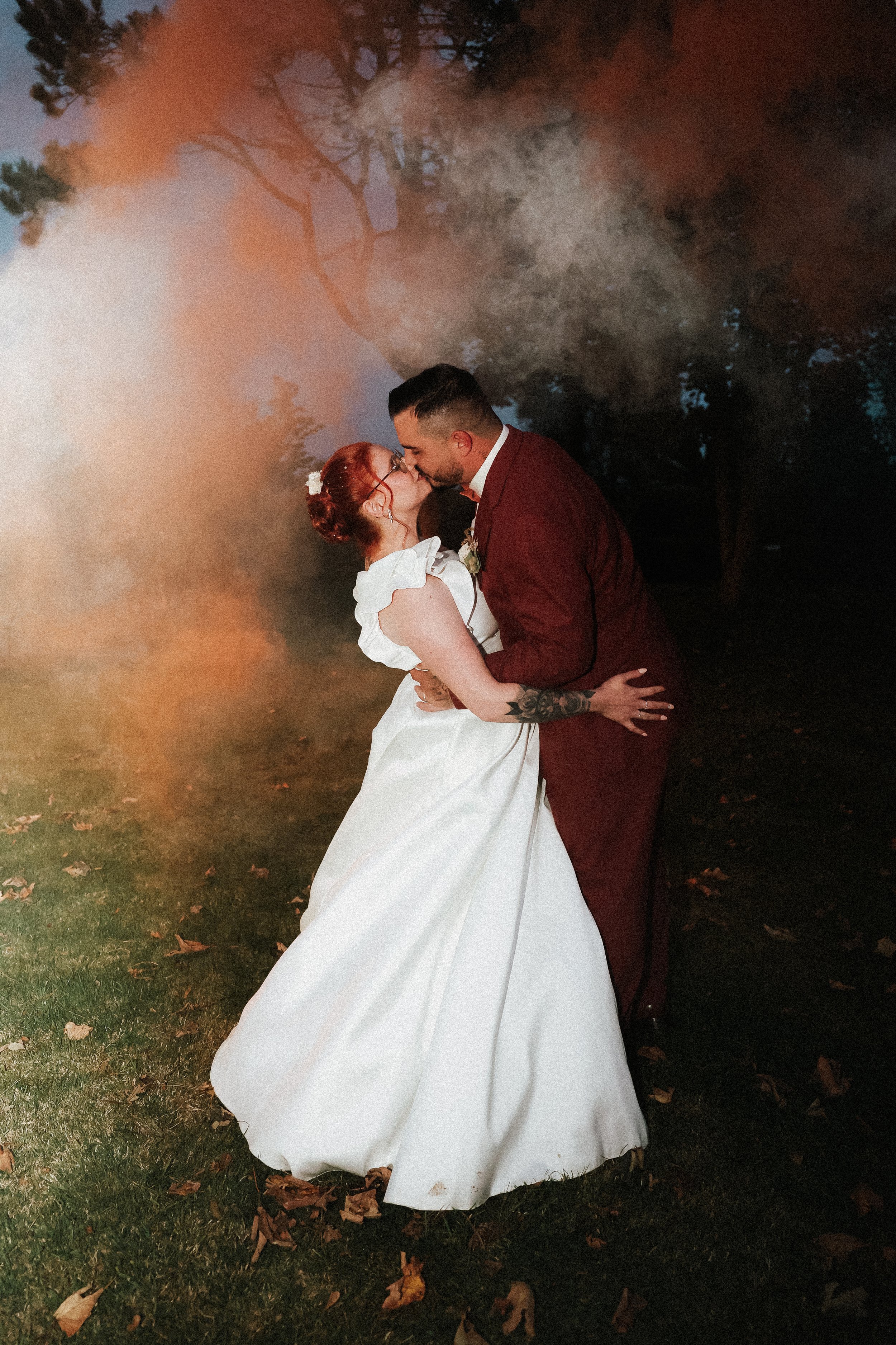 Un couple en robe de mariage s'embrasse dans un parc avec une atmosphère brumeuse et des arbres en arrière-plan.