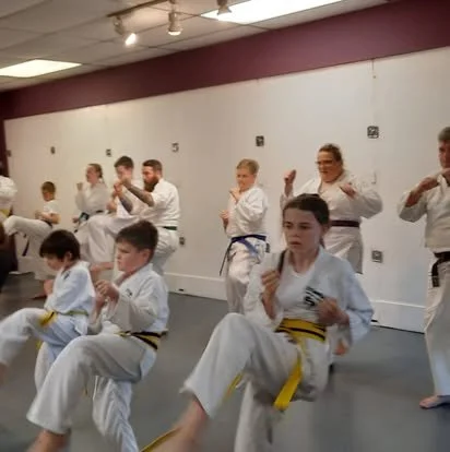 Kids and adults in martial arts uniforms practicing punches and kicks in a dojo.