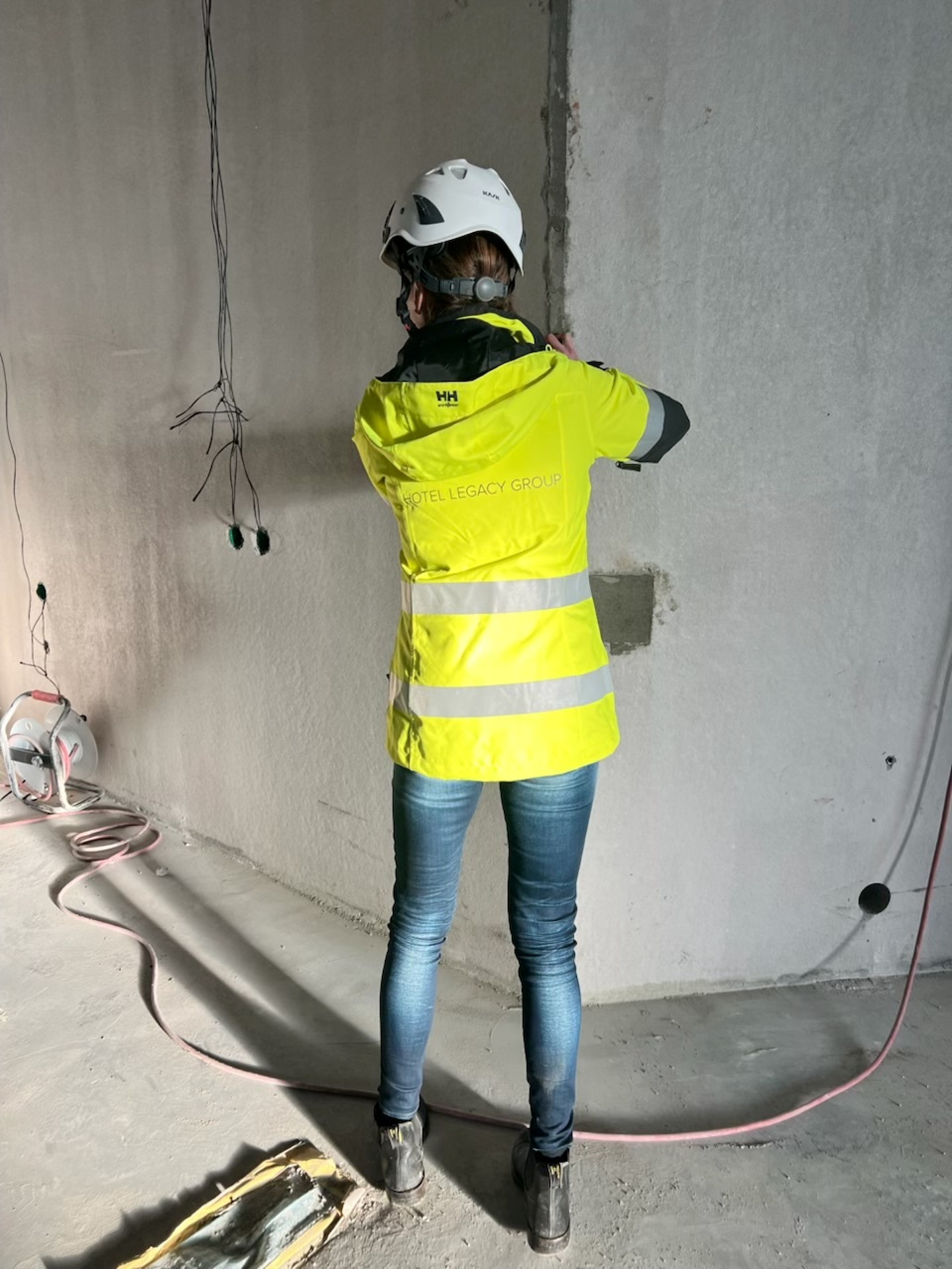 Person i byggarbetskläder och hjälm står med ryggen mot kameran och jobbar på en vägg på en byggarbetsplats.