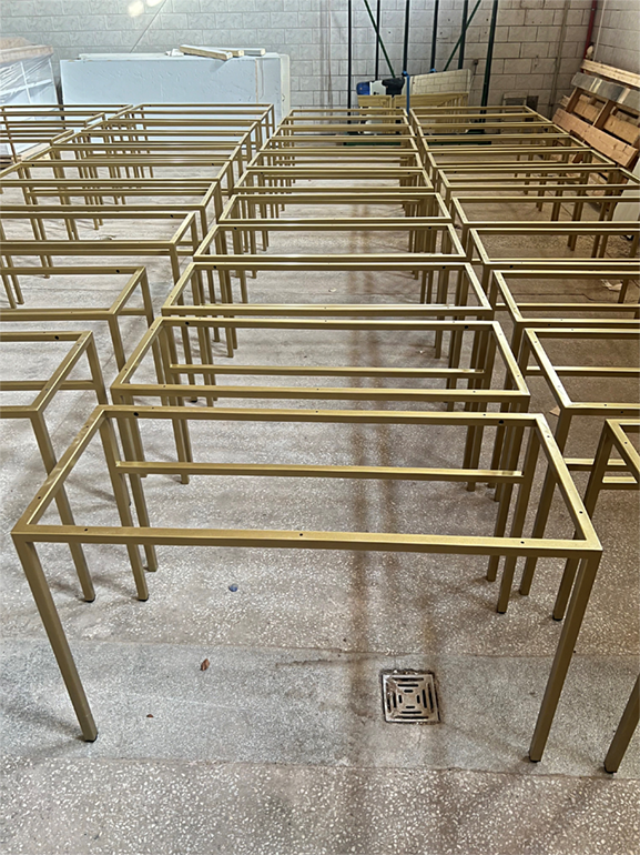 Rader av metallramar för möbler eller annan konstruktion i ett verkstad eller lager, stående på en betonggolv.