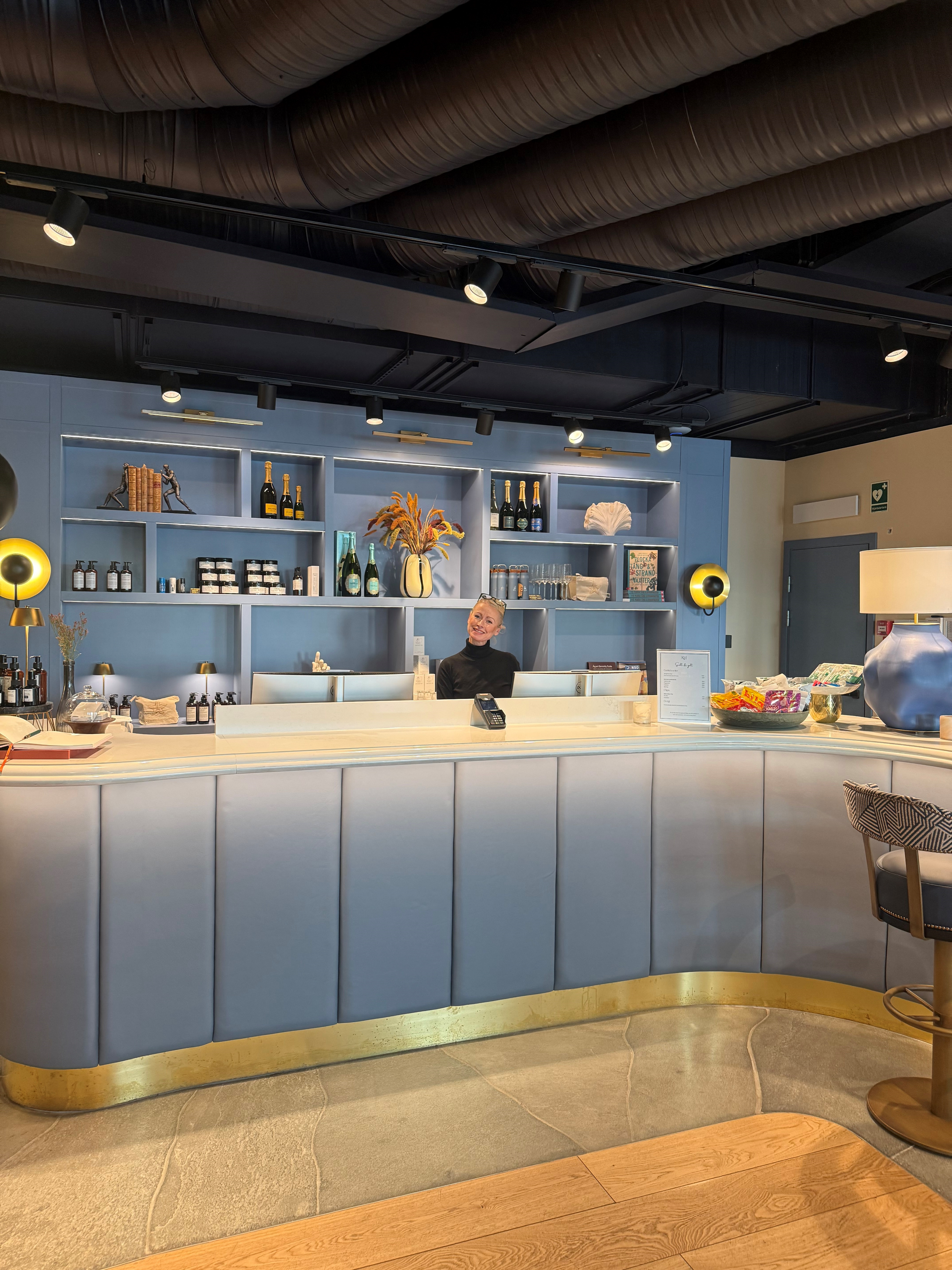 En bar eller reception med en blå barstaty och en kvinnlig personal som ler.