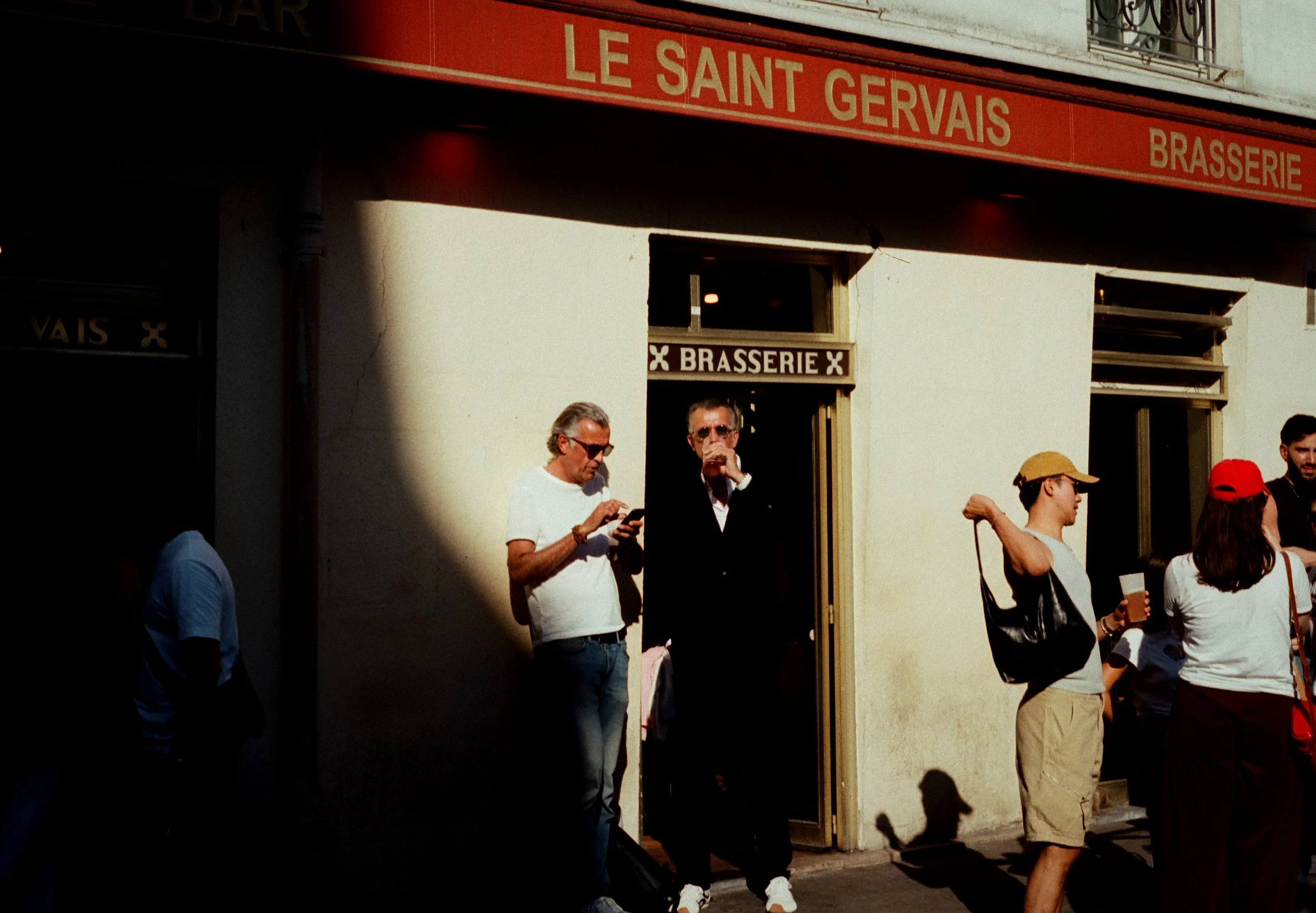 Image de plusieurs personnes debout à l'extérieur d'un bâtiment avec une enseigne rouge indiquant 'Le Saint Gervais Brasserie'.