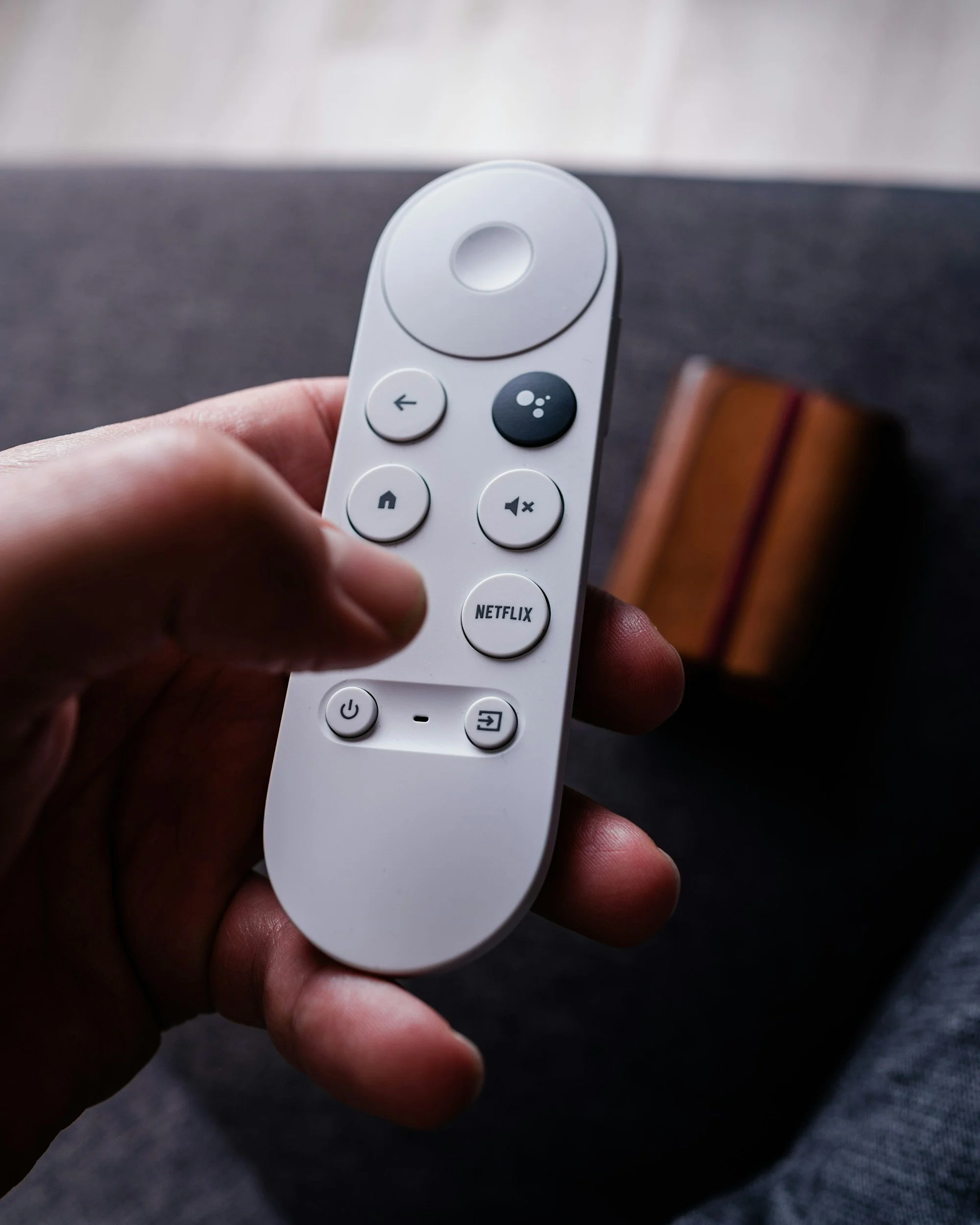 A hand holding a white air conditioning remote control with various buttons, including a Netflix button, against a blurred gray background.