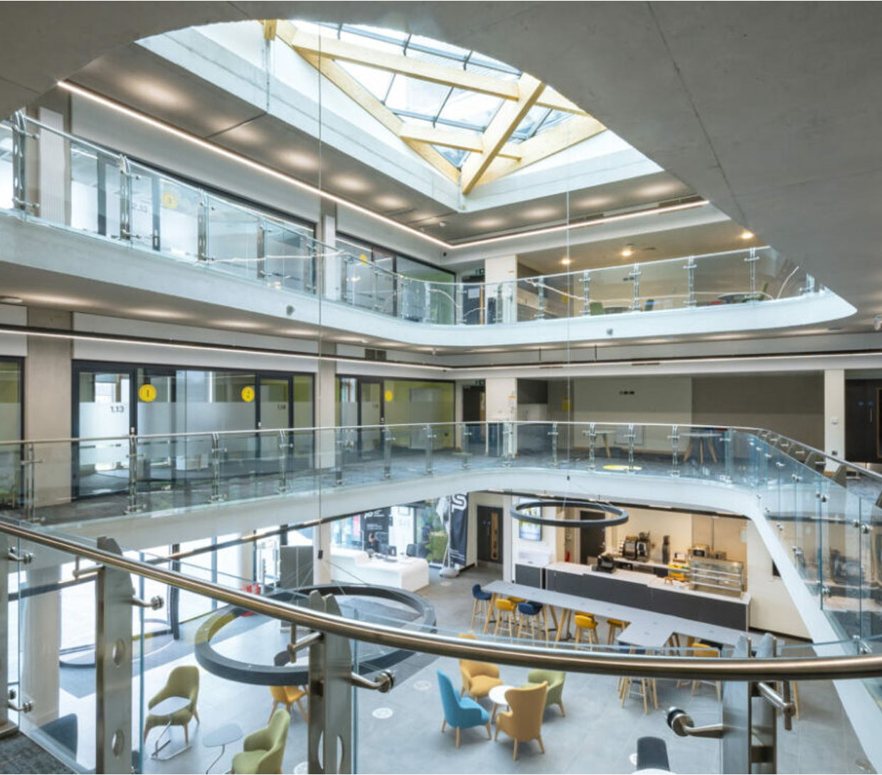 Interior of a modern multi-story office building with glass balconies, multiple floors, a skylight, and a lounge area with chairs and a reception desk.