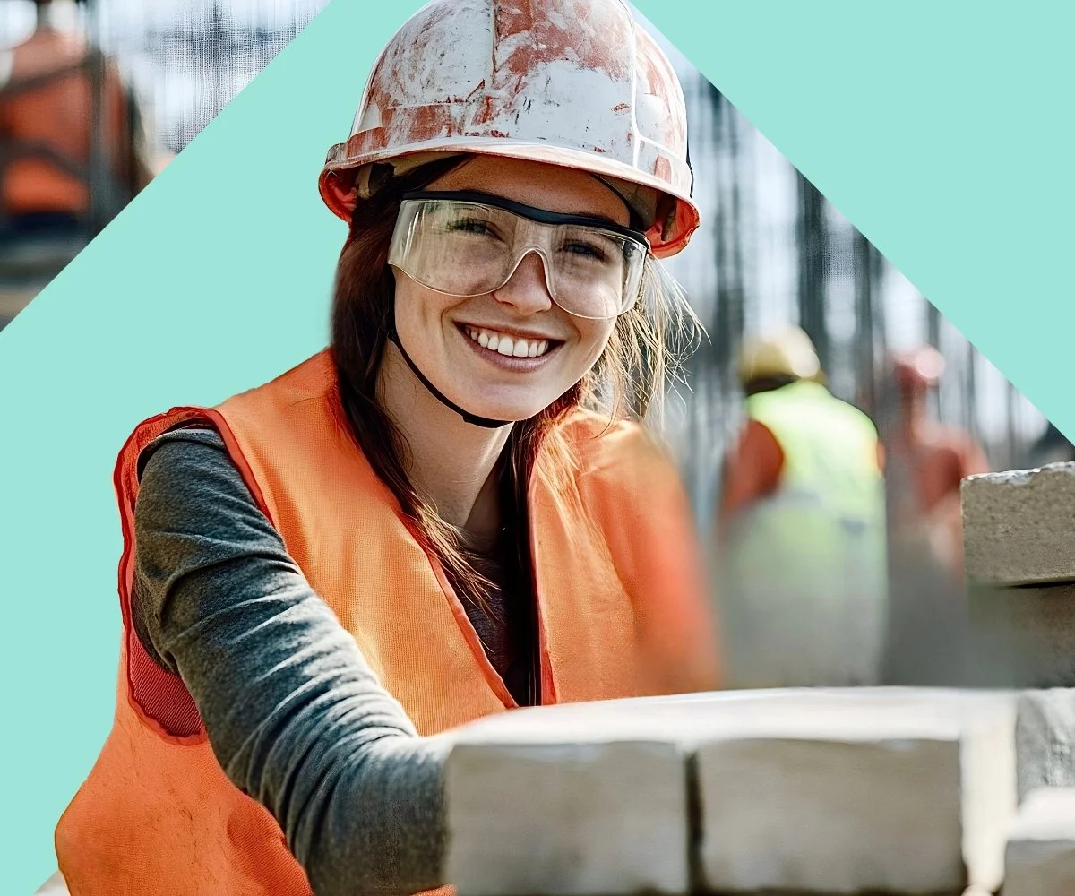 Smiling female construction worker wearing safety helmet and glasses at a building site.