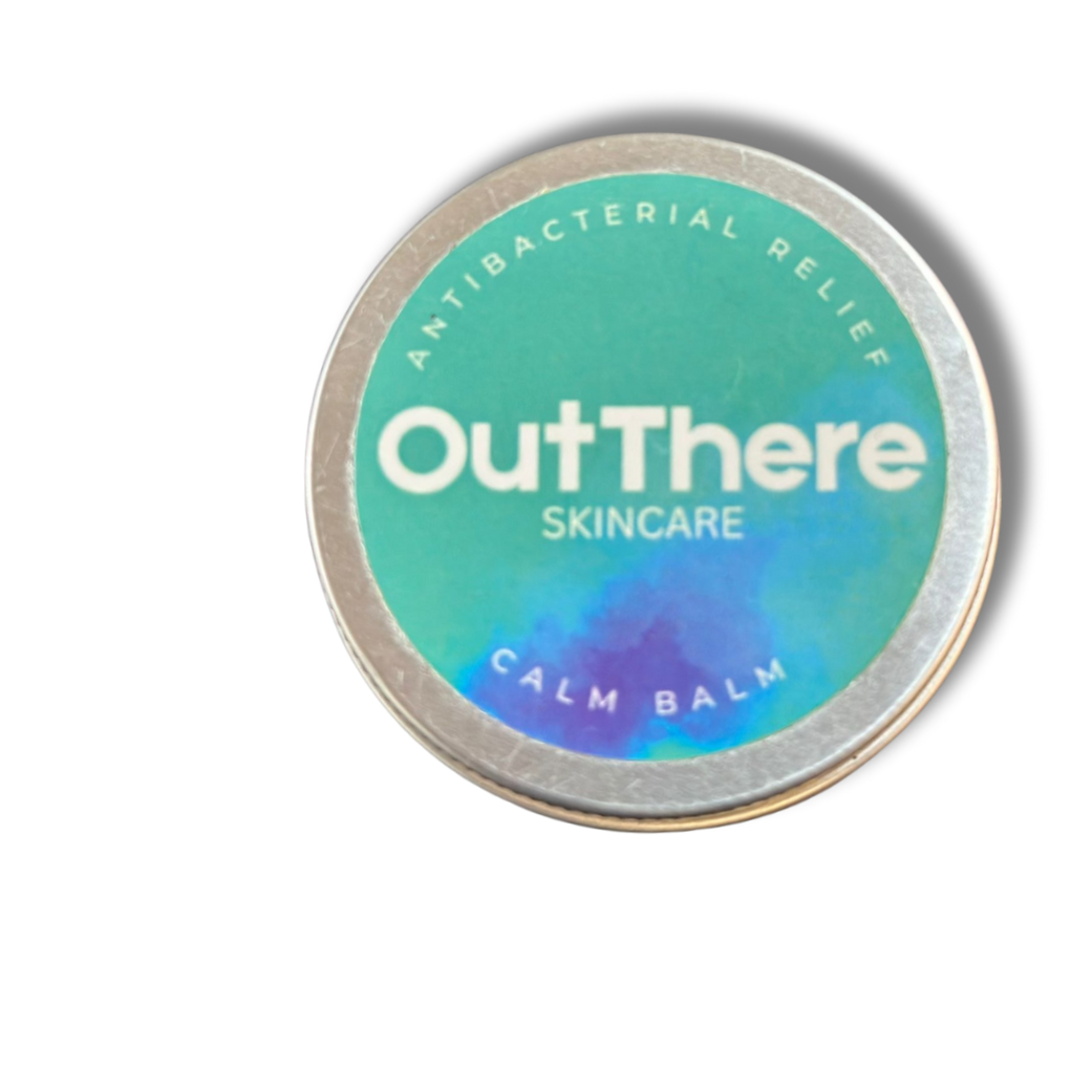 A round tin container with a holographic label that reads, 'A natural antibacterial relief Out There Skincare Calm Balm'.