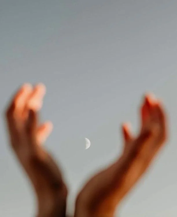 Outstretched hands framing a crescent moon in the sky.